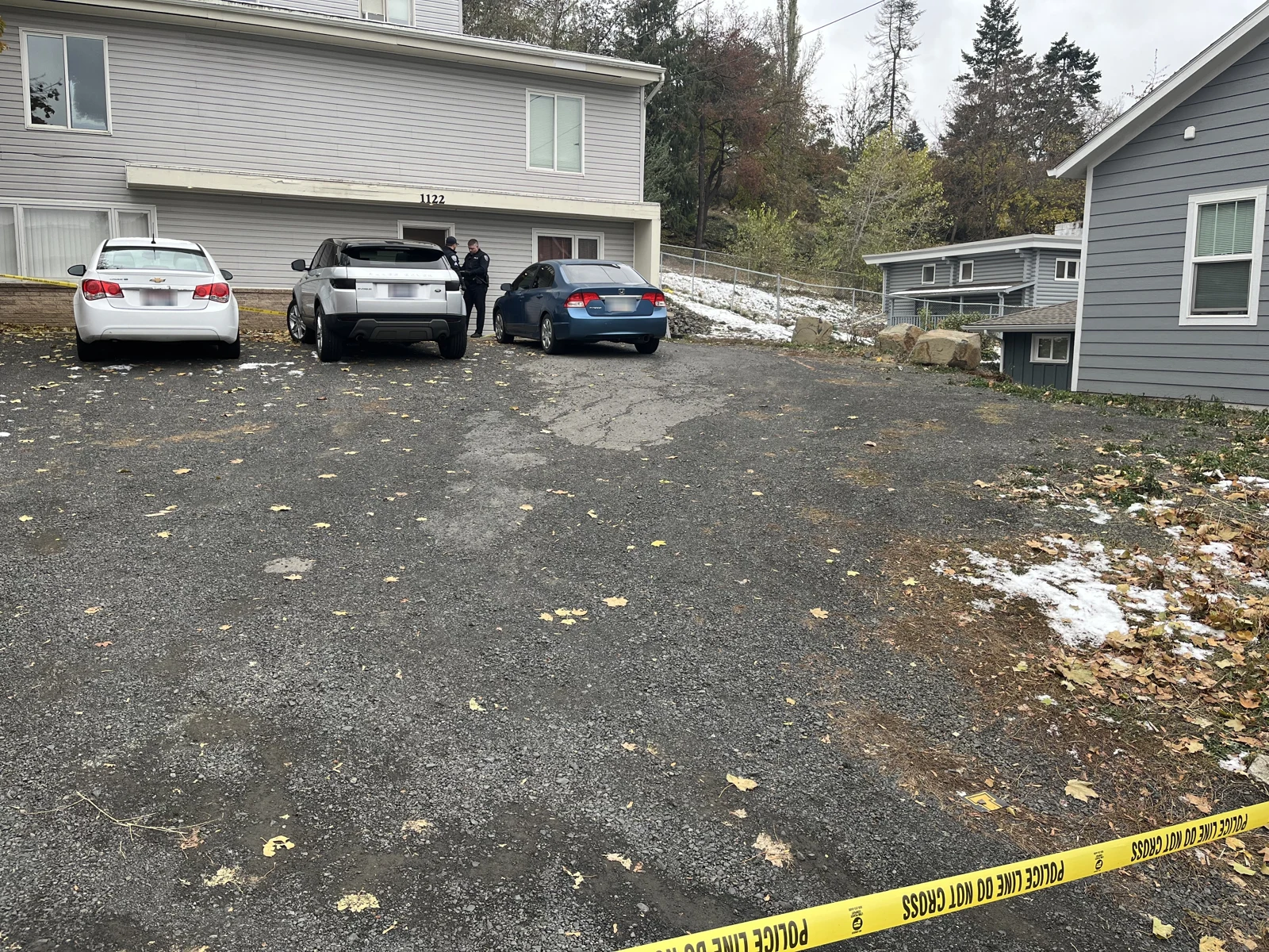 Three vehicles parked outside a gray house marked 1122, with a person near the entrance and patches of snow at the driveway edges.