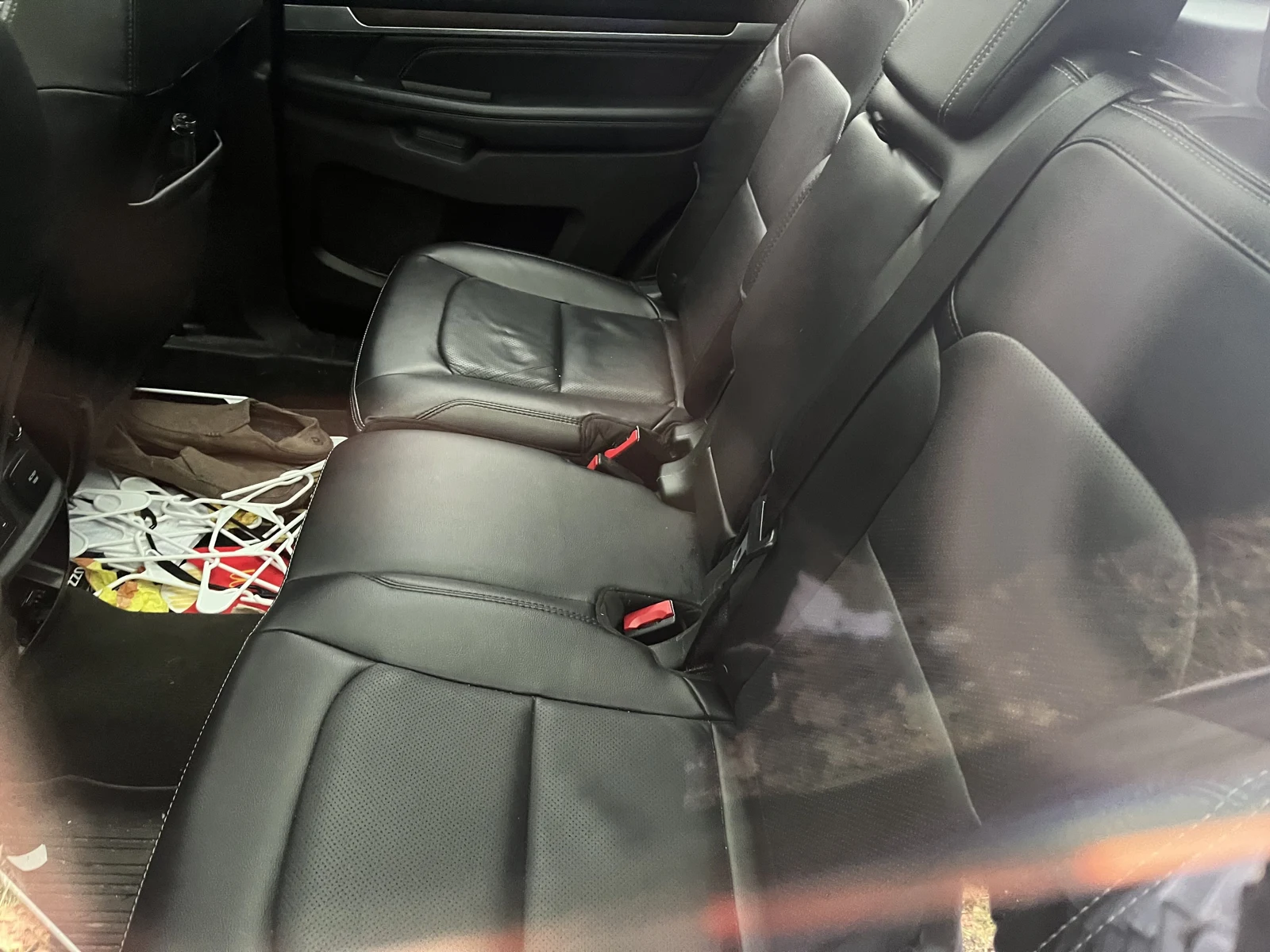 Black leather rear bench seat and footwell inside a vehicle, with loose white cords and colorful items on the floor.