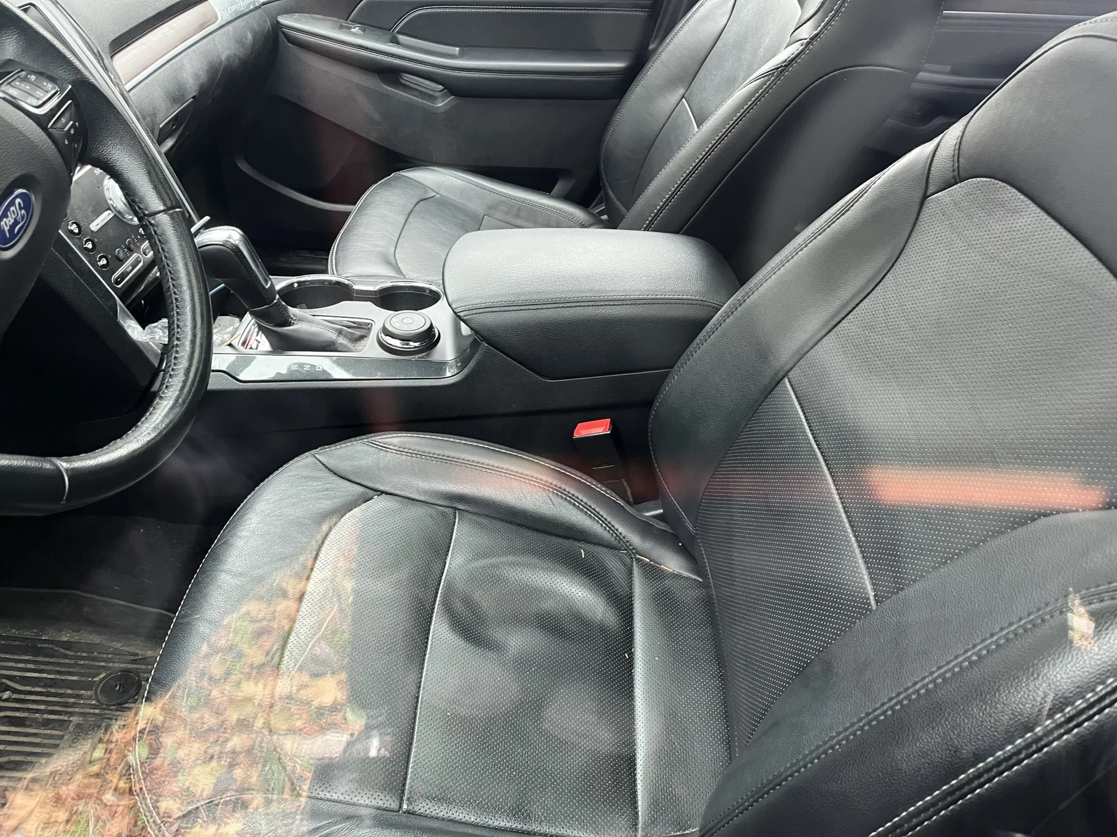Black leather front seats, steering wheel, gear selector and center console inside a vehicle, viewed through reflective glass.