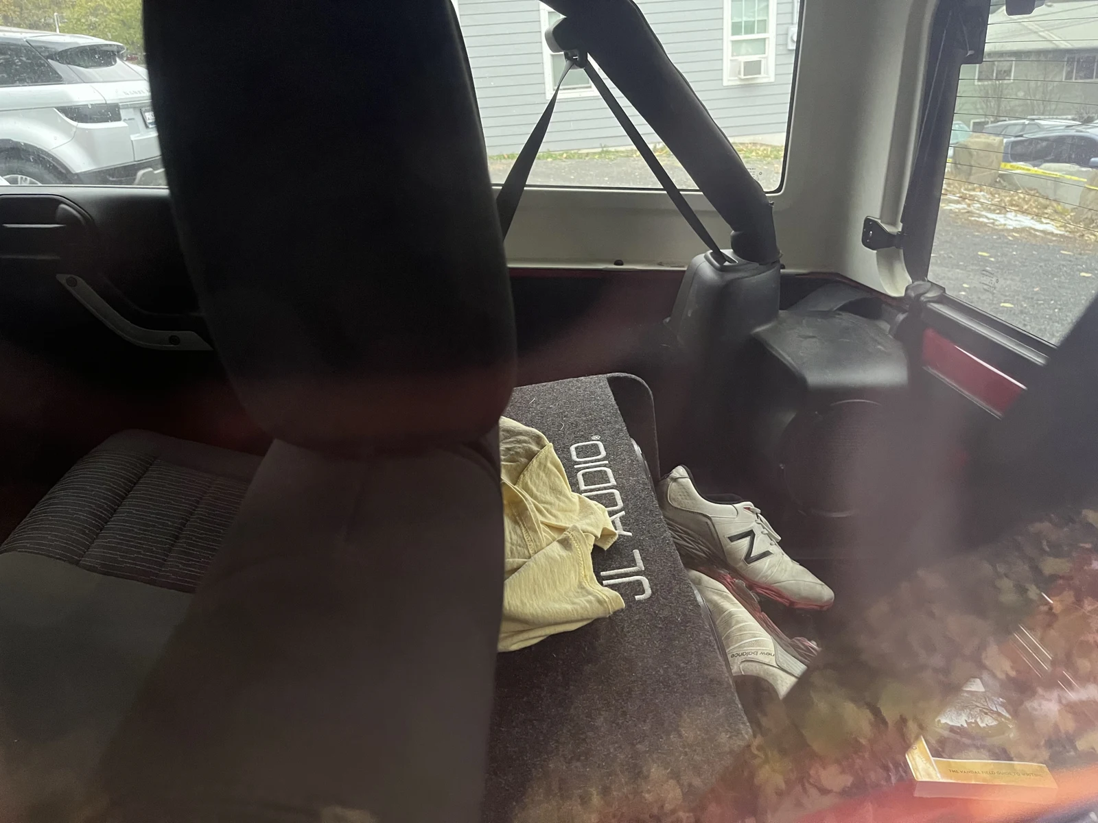 View through vehicle glass into a rear seating area with a hanging seat belt, pale fabric and a light-colored sneaker.