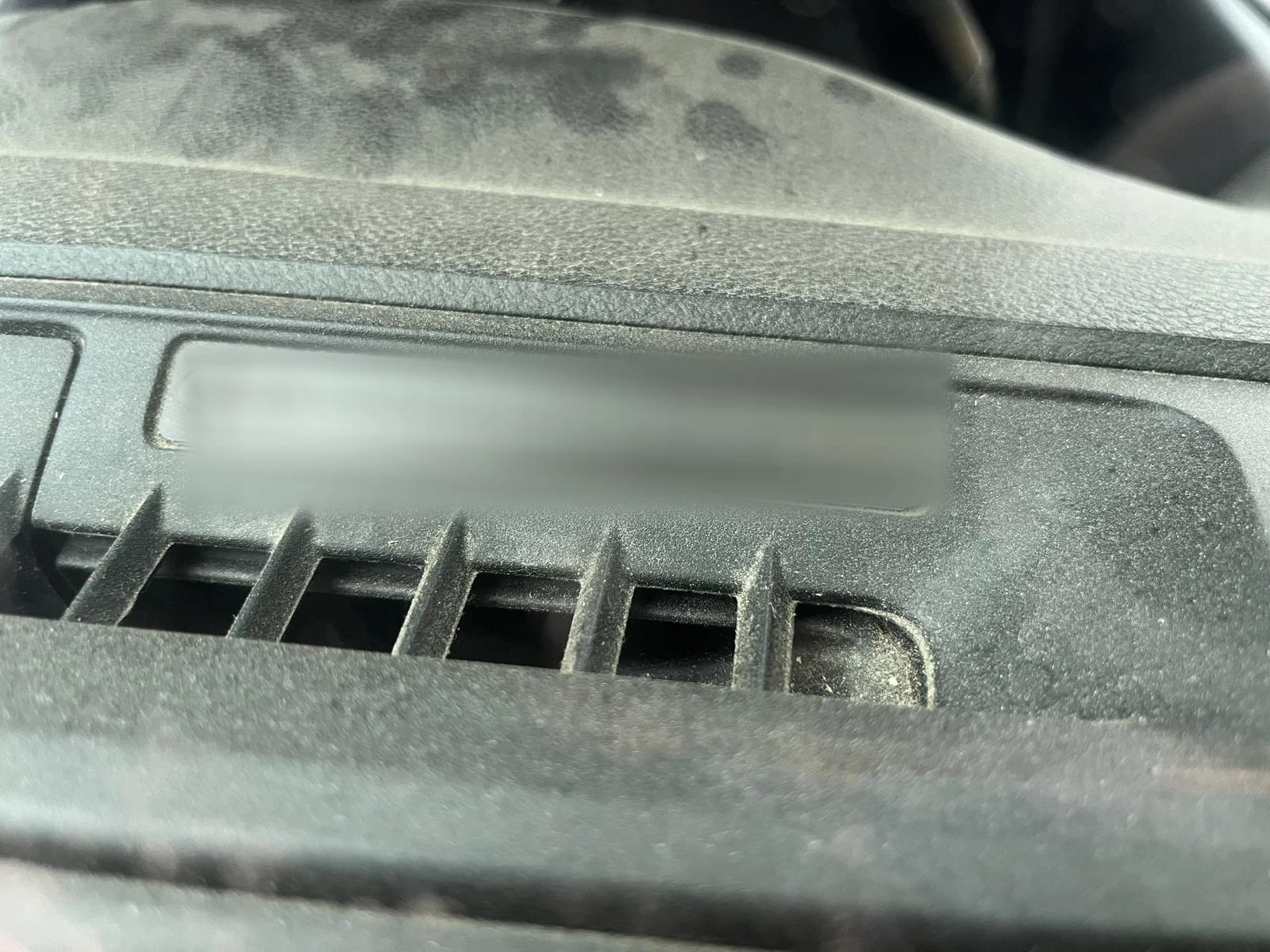 Close view of a dusty dashboard identification area with the identifying text blurred in the source image.