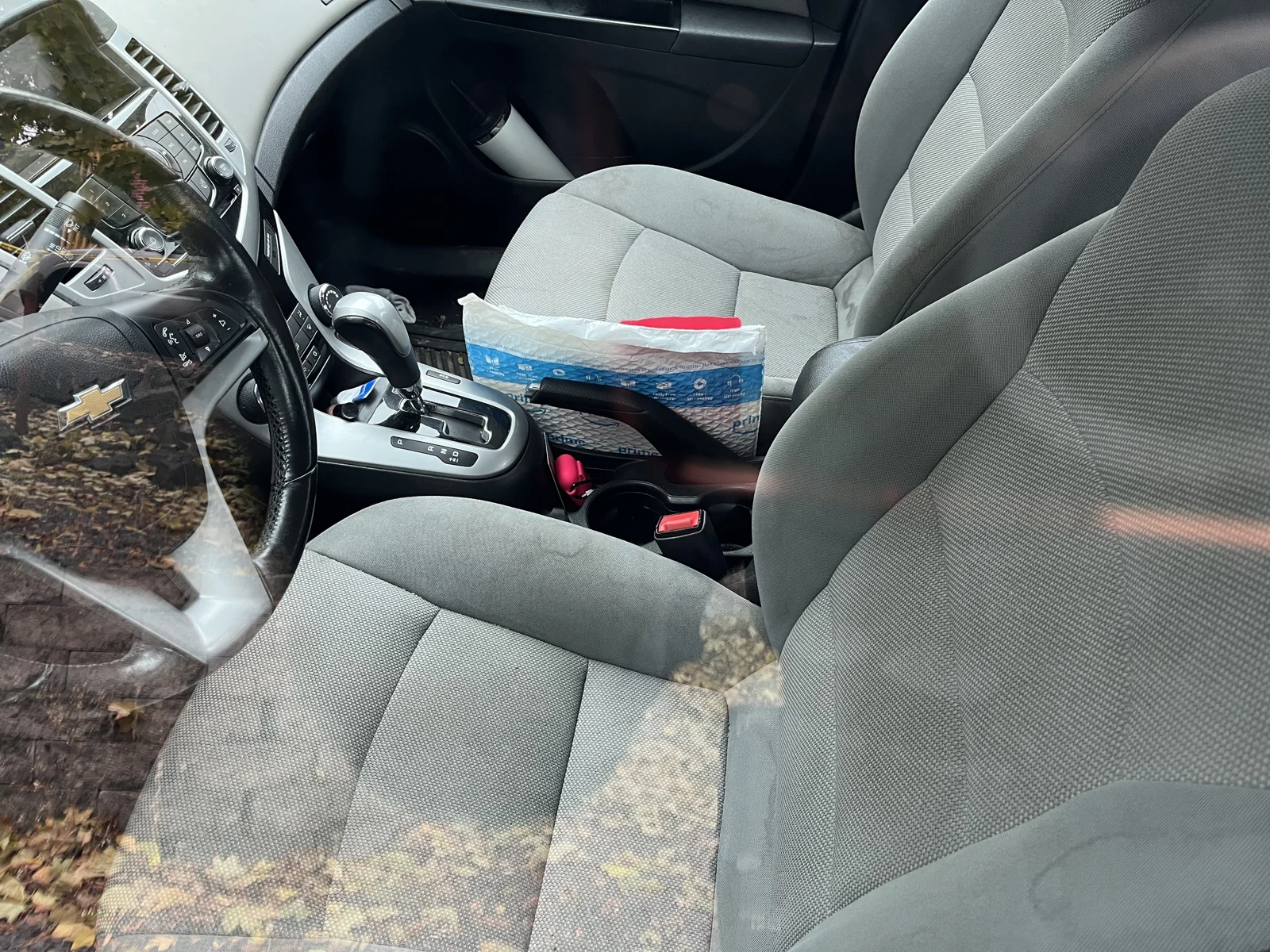 Gray front seats and Chevrolet steering wheel, gear selector and a tissue box on the center area, viewed through glass.