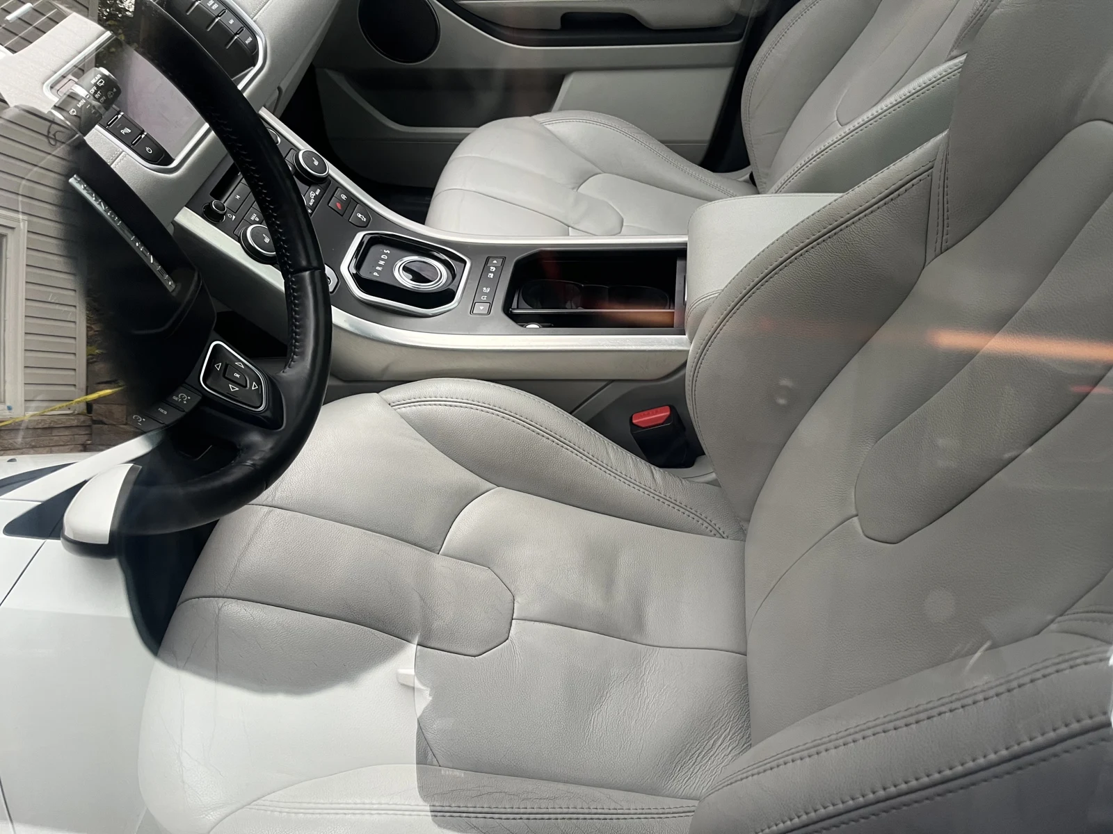 Light leather front seats, steering wheel and center console with a round gear selector and open storage compartment.