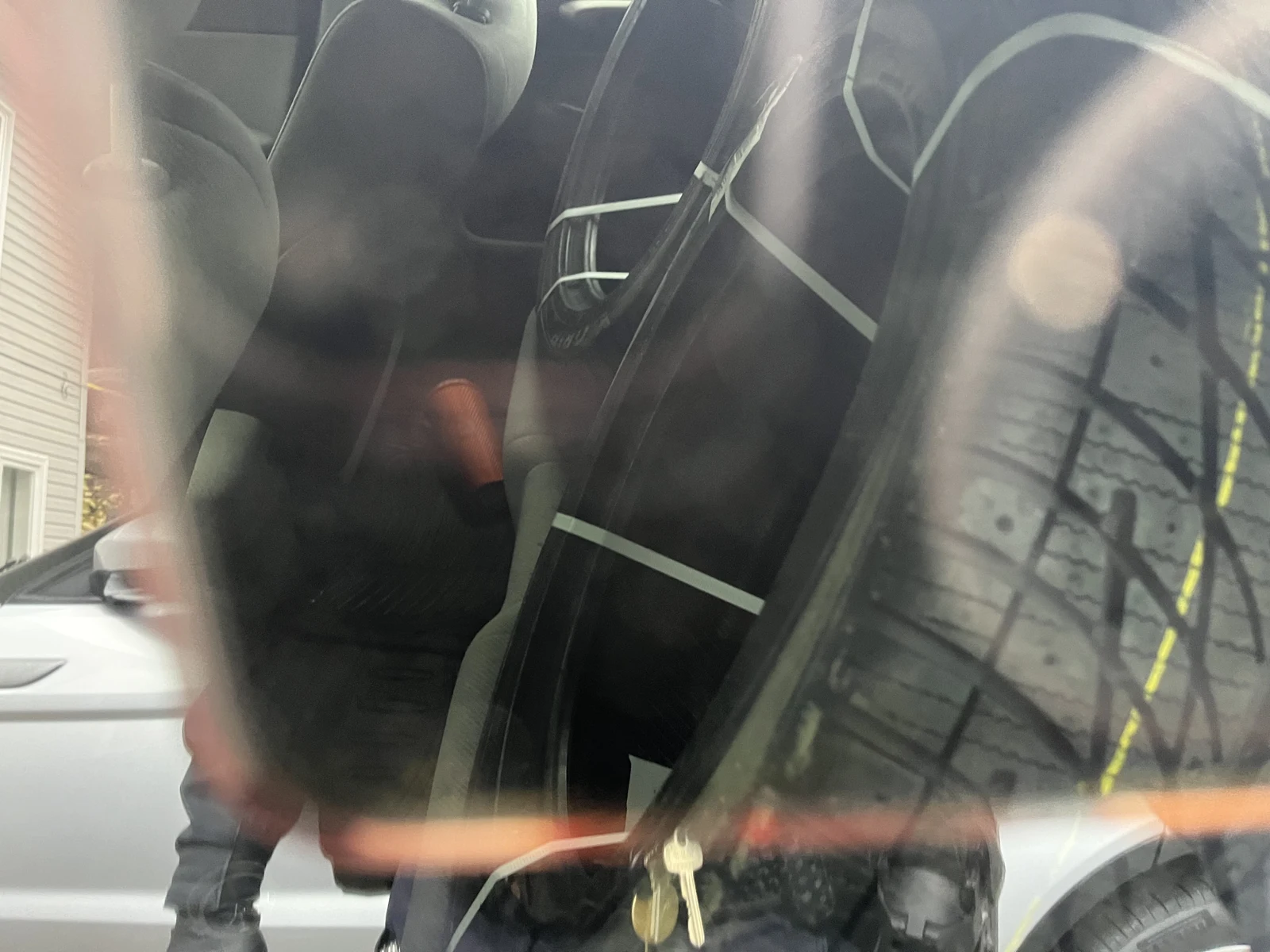 View through reflective glass of a large tire stored upright inside a vehicle, with straps and dark seating behind it.