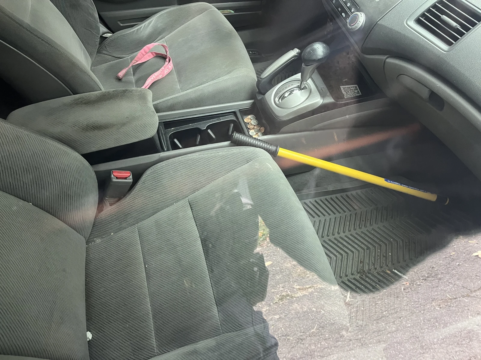 Gray vehicle front seats and center console with a yellow-handled object extending across the passenger area and a pink strap on the driver seat.