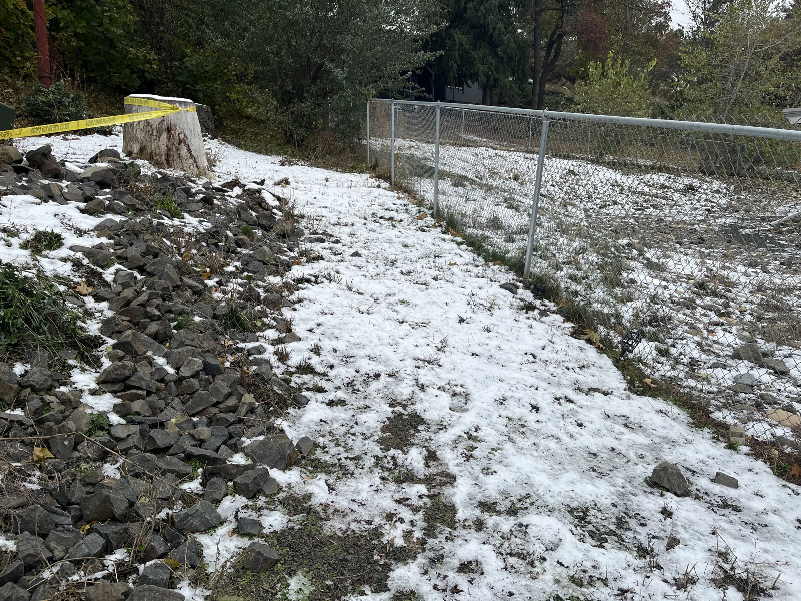 Rocky slope with patchy snow, a chain-link fence and a taped tree stump at the upper left.