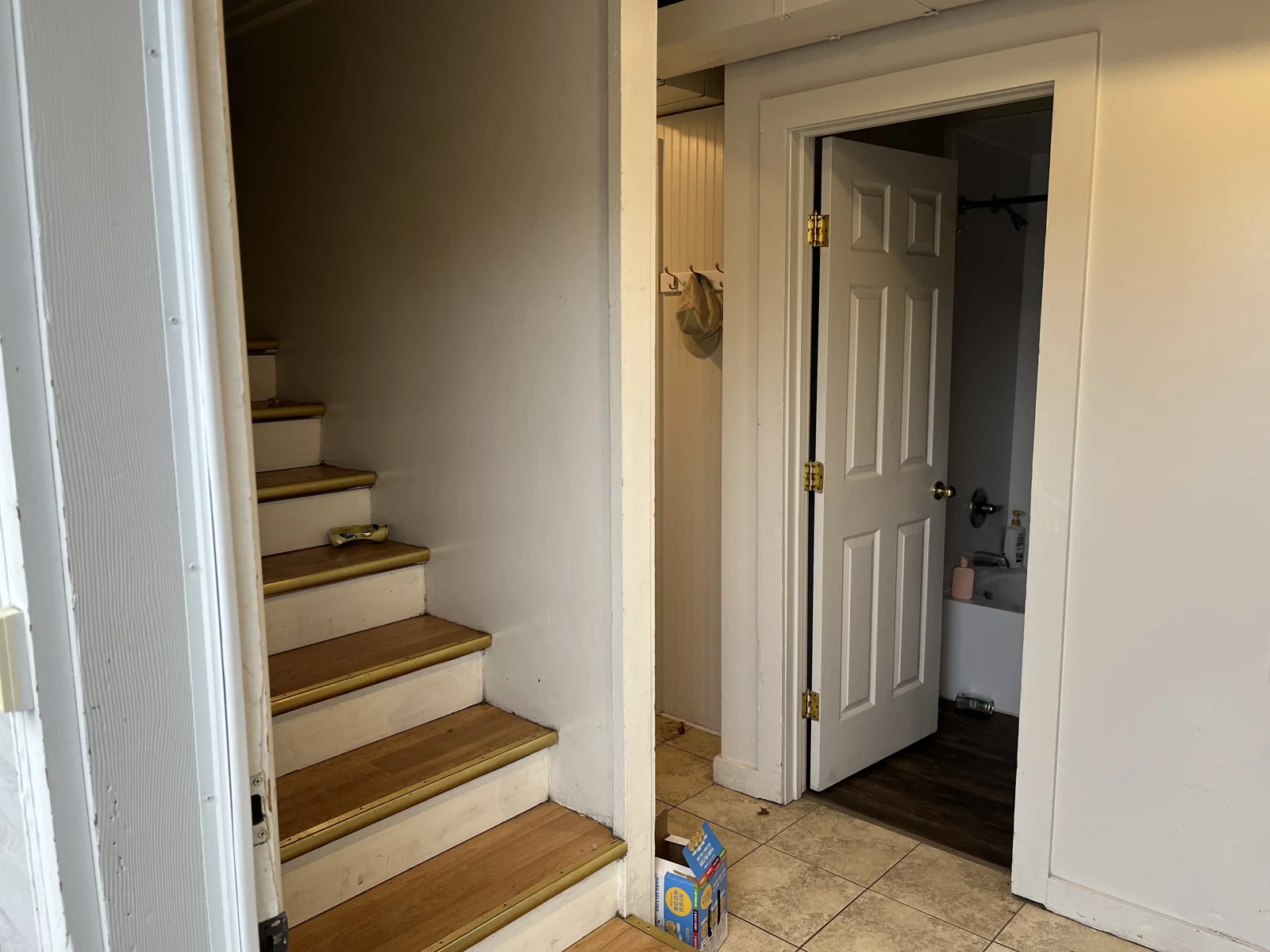 Entry hallway with wooden stairs, tile flooring and an open bathroom doorway with toiletries visible.
