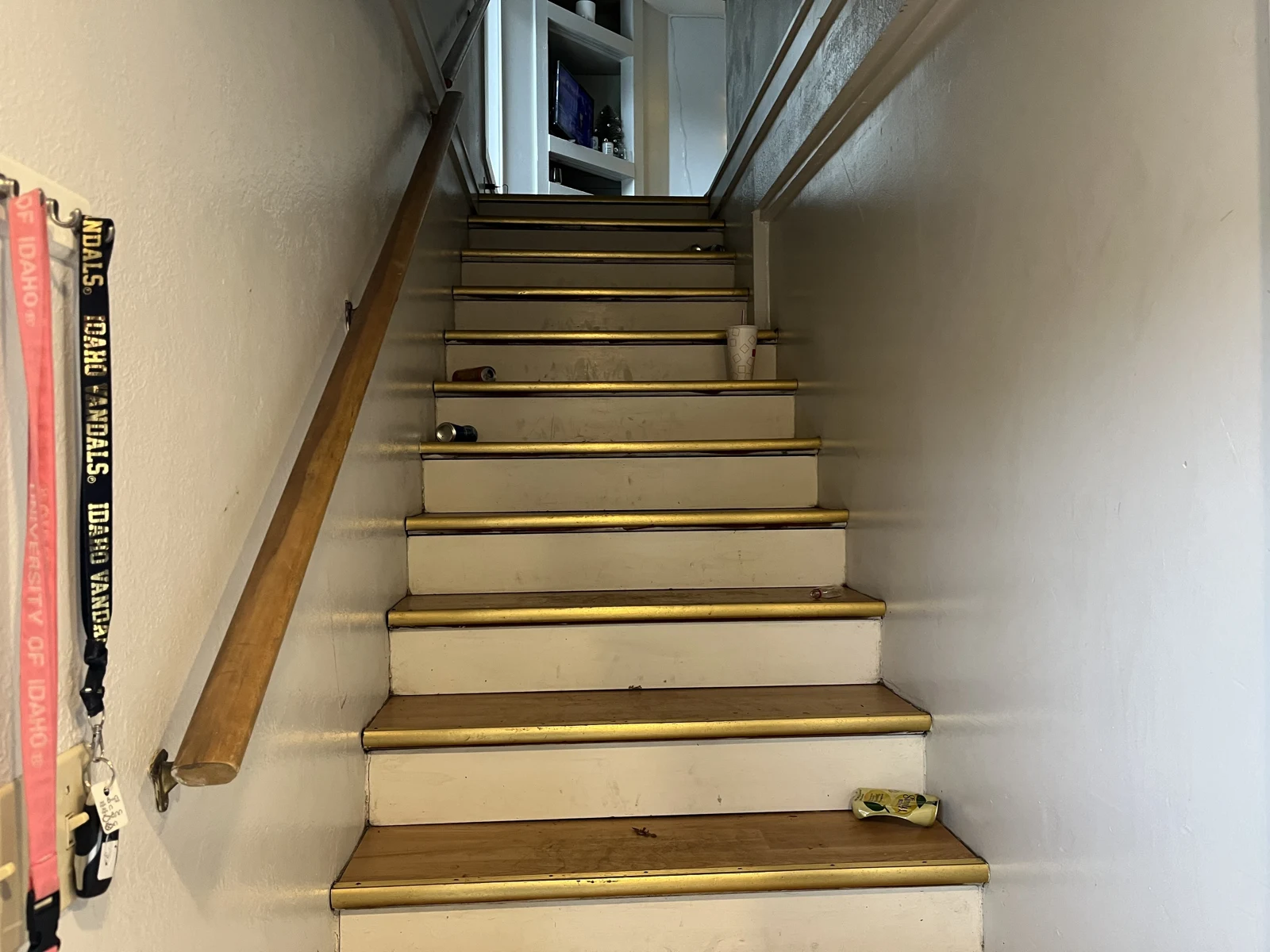 Wooden staircase with handrails, hanging lanyards, a disposable cup and small objects on several steps.