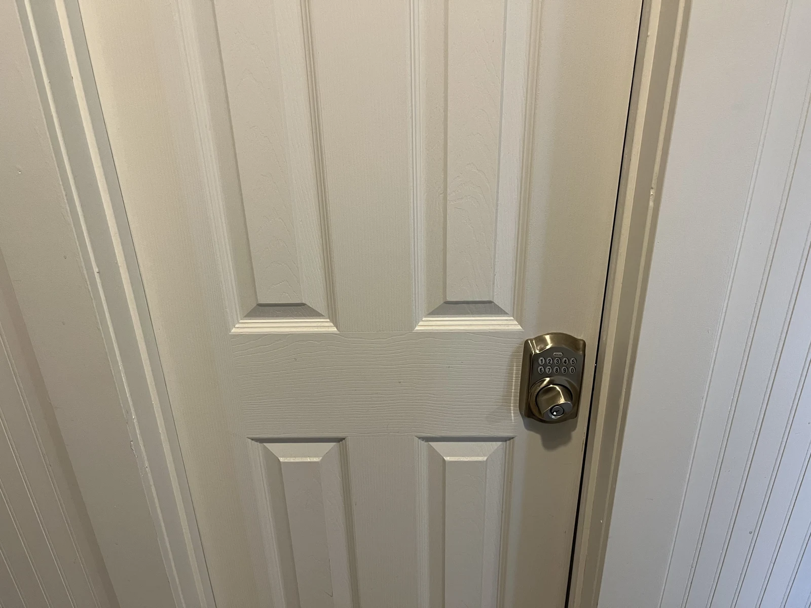 Close view of a closed white paneled door with a metallic keypad door lock.