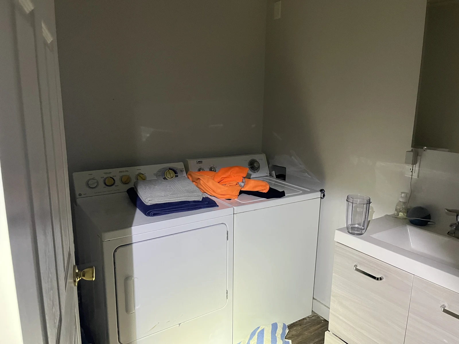 White washing machine and dryer with clothing on top, beside a bathroom sink cabinet.