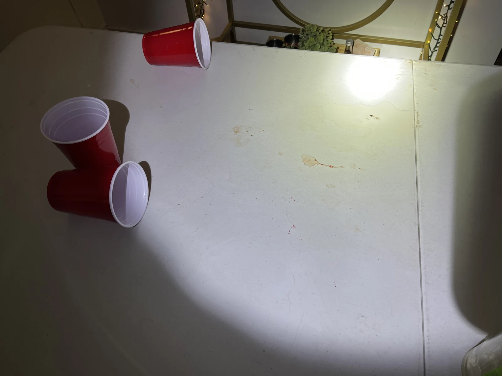 Close view of a white tabletop with several red cups, faint marks and a flashlight beam.