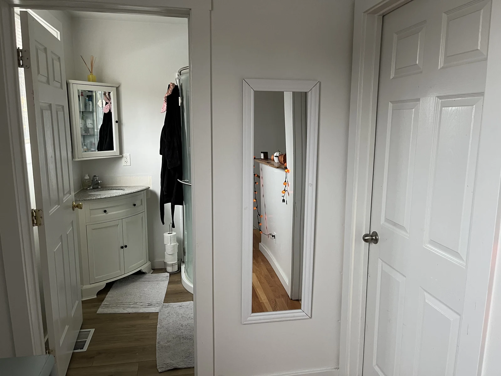 Upper hallway with a narrow full-length wall mirror, closed white door and open bathroom doorway showing a curved sink cabinet.
