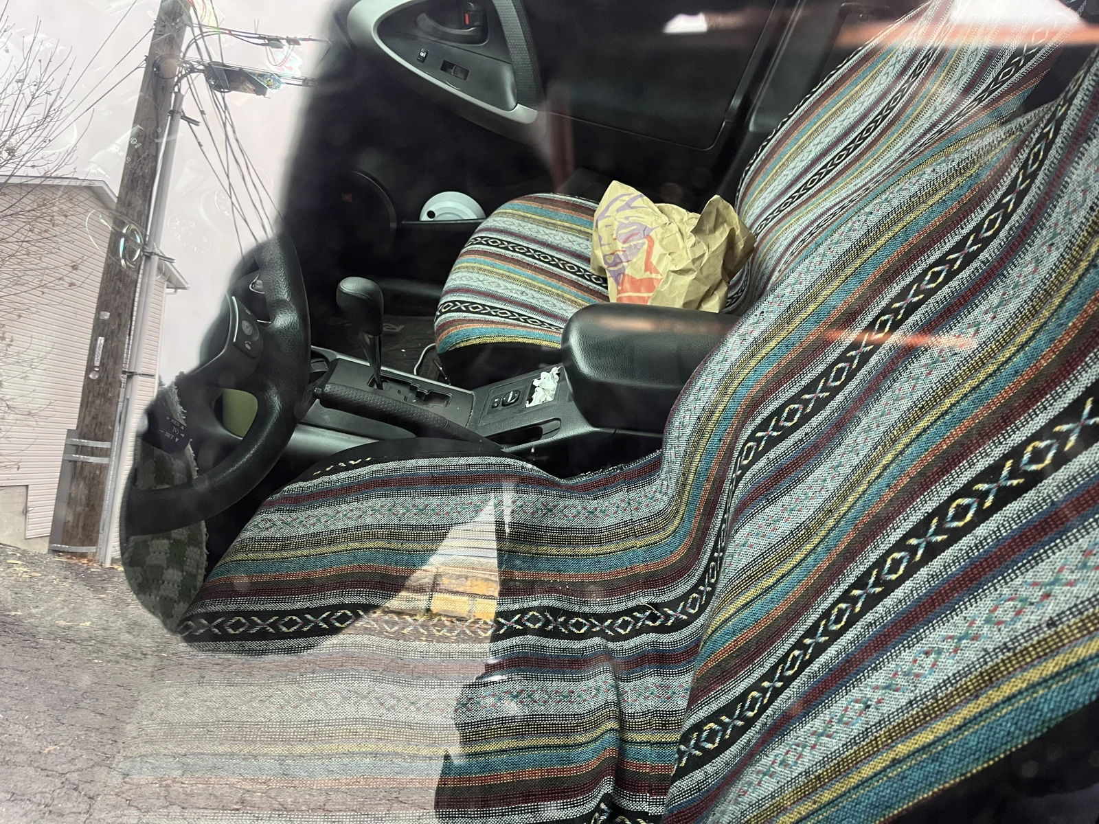 Vehicle front seats with multicolored striped fabric covers, center console and a yellow bag on the passenger seat.