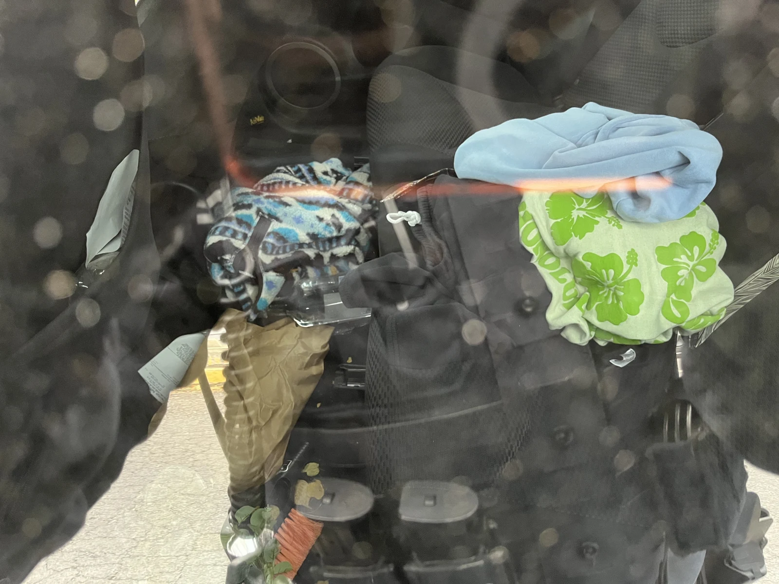 View through reflective vehicle glass of patterned fabric and bags, including light-blue and green floral material.