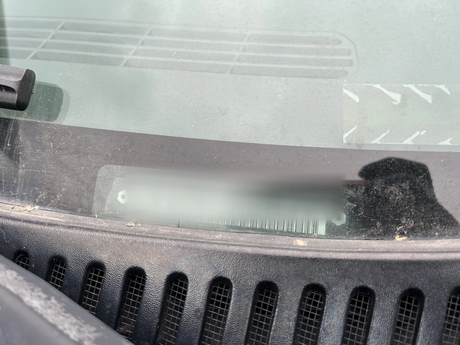 Close view through a vehicle windshield of a blurred identification area and dashboard vent.