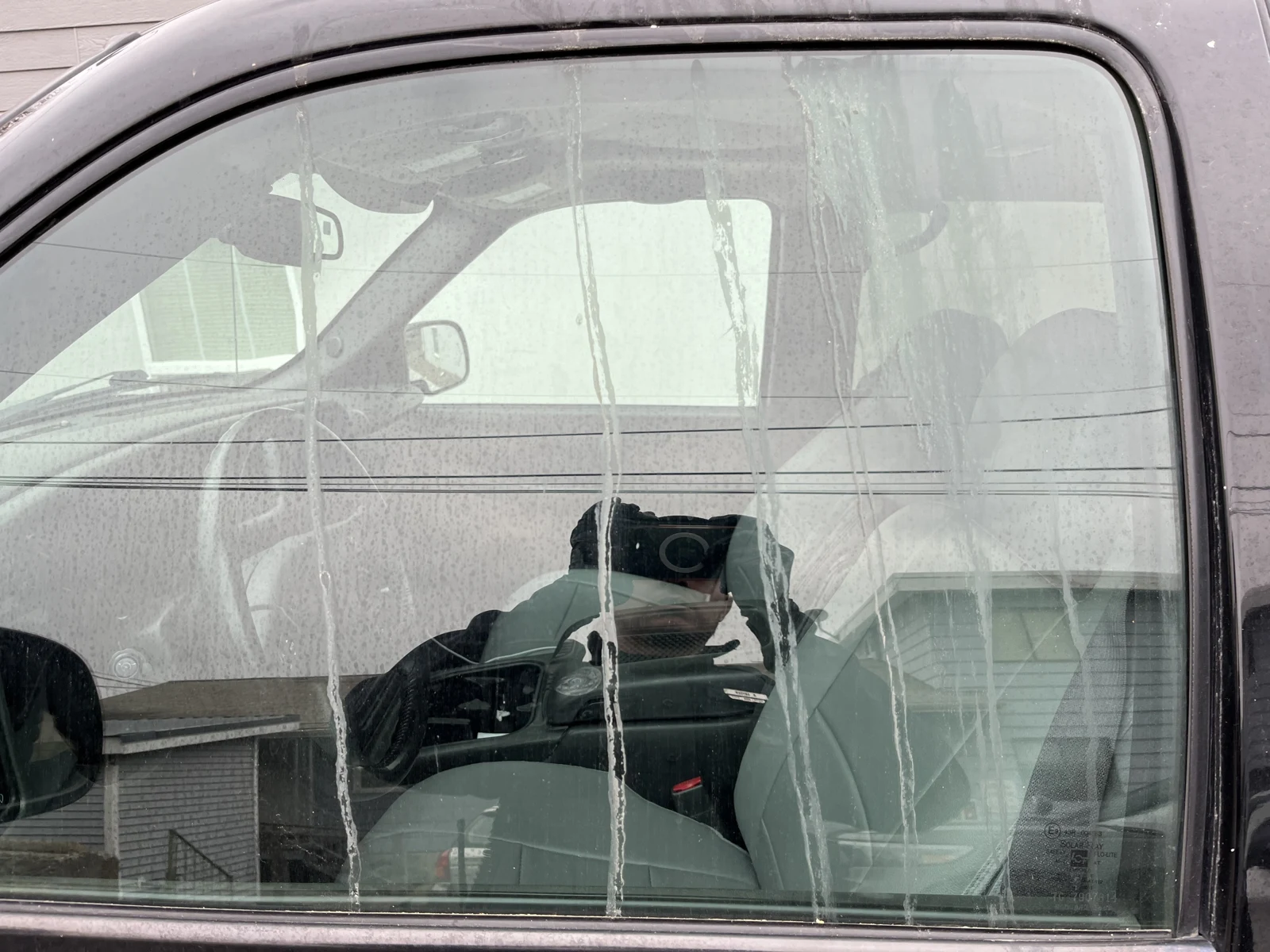 Vehicle side window with long pale vertical streaks and reflections, with gray seats and steering wheel visible inside.