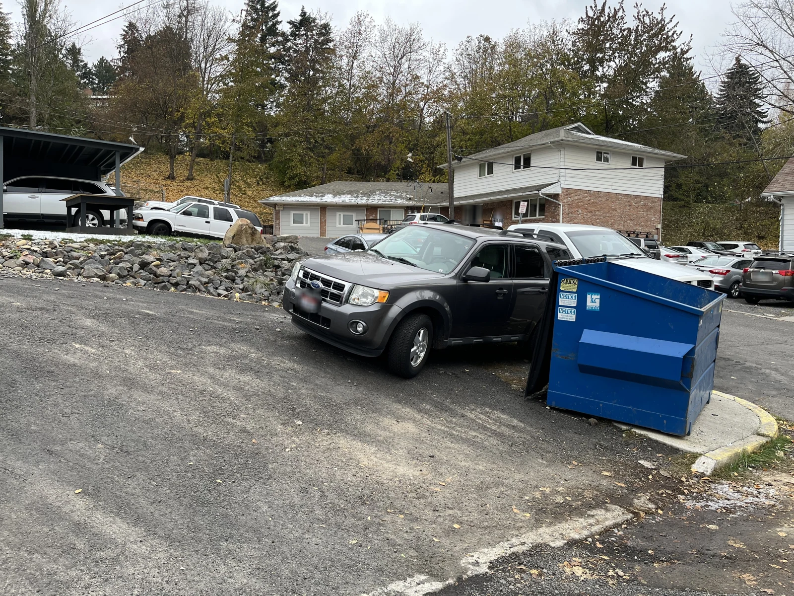 Gray pickup truck beside a blue dumpster on a sloping residential street.