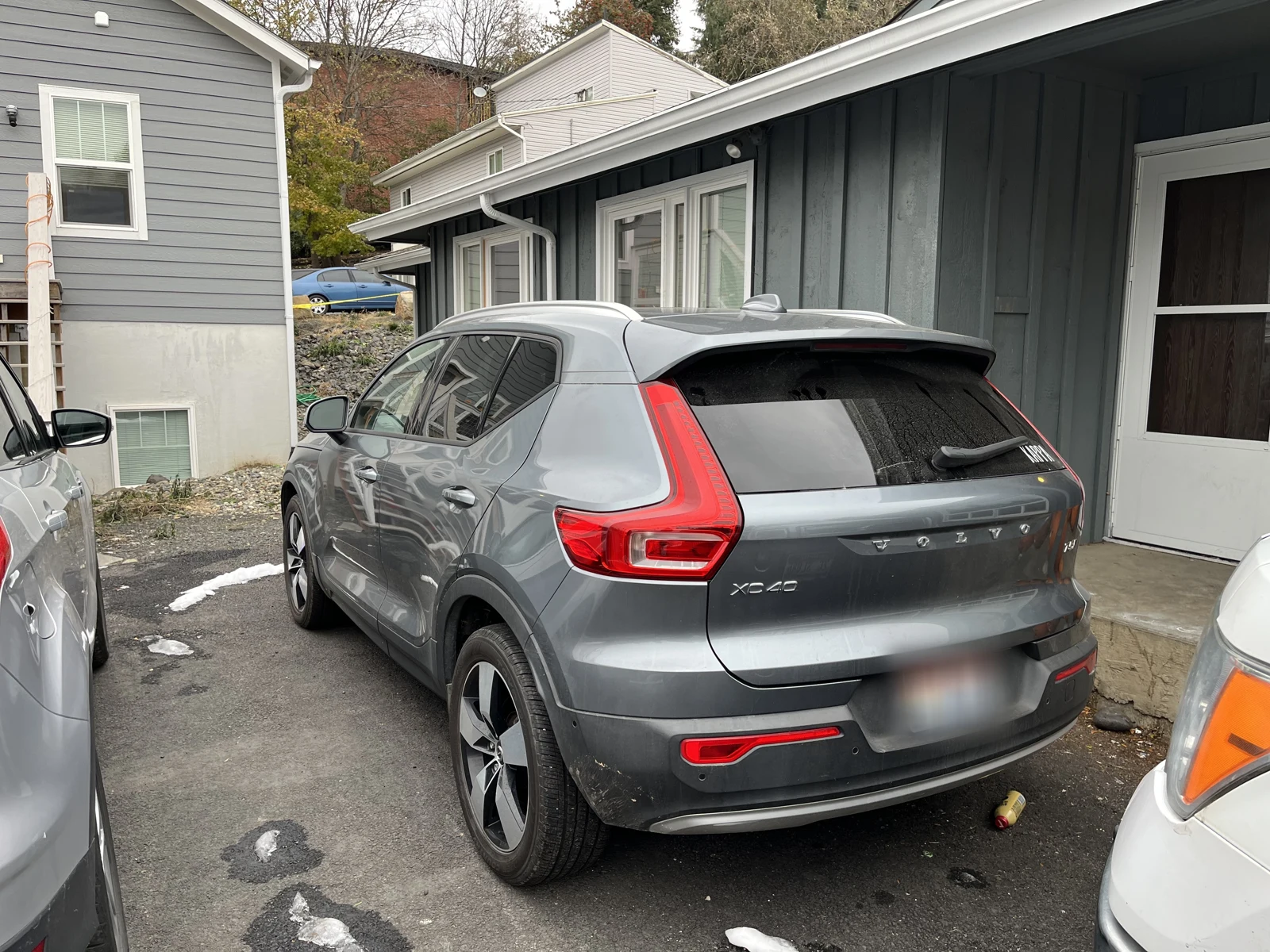 Rear-side view of a gray Volvo XC40 with a blurred plate, parked beside a dark-sided building.