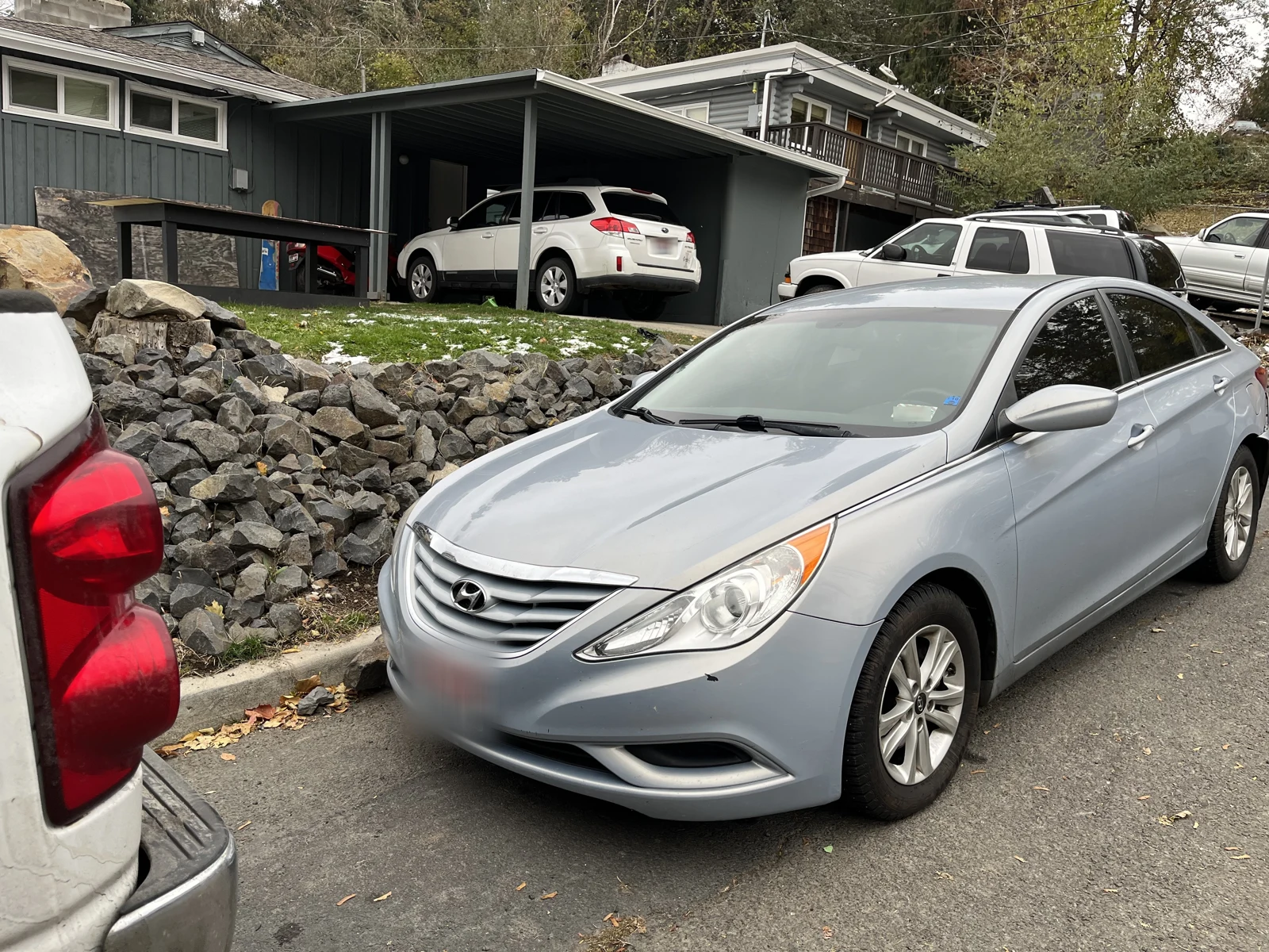 Front-side view of a silver Hyundai sedan parked below a rocky retaining slope and a carport.