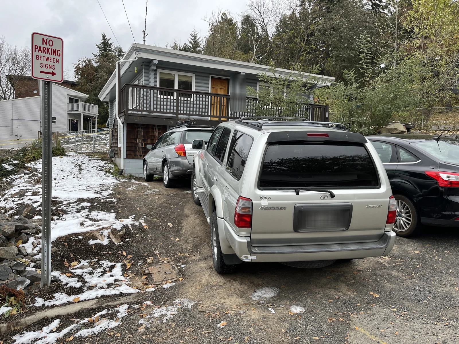 Rear of a silver Toyota SUV near a No Parking Between Signs sign, with a raised balcony and snow beside the driveway.