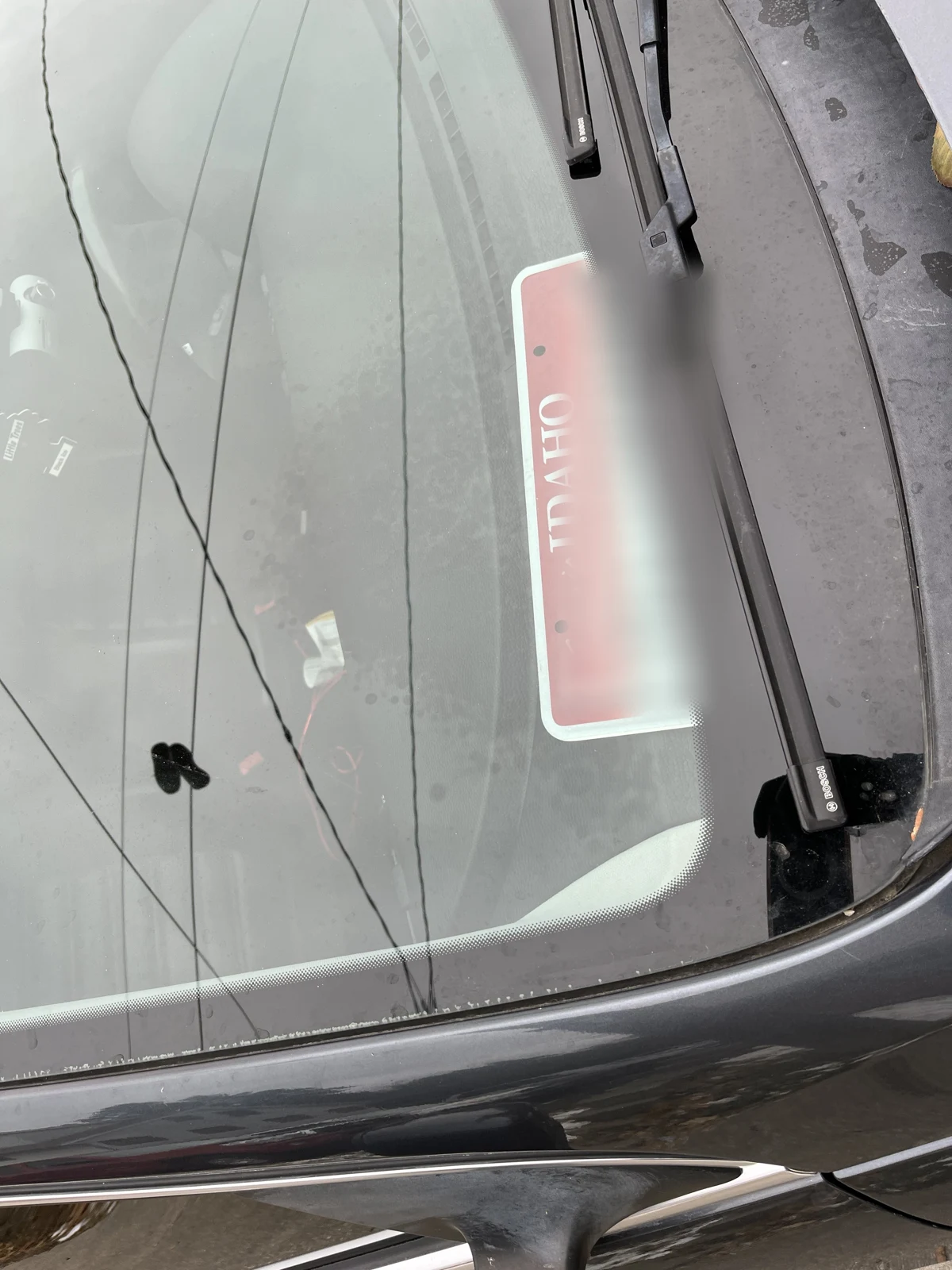 Angled windshield photograph with an Idaho plate or placard on the dashboard, identifying characters blurred, and wipers visible.
