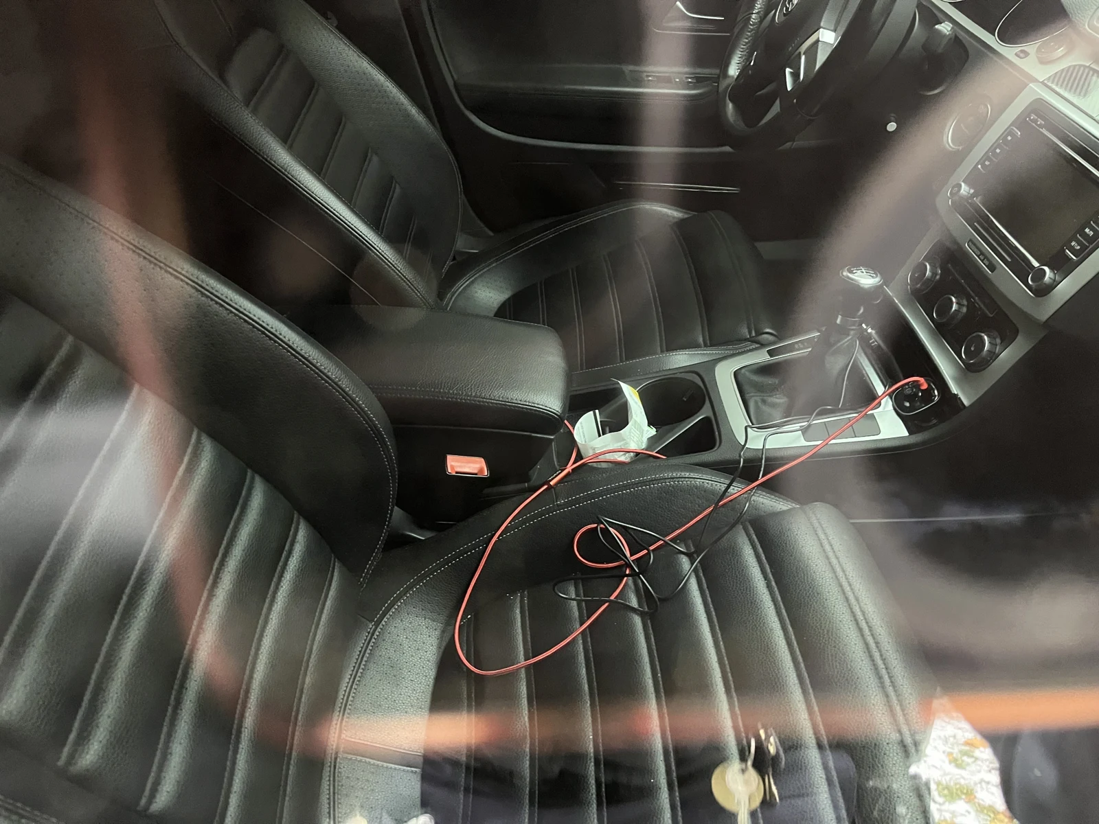 Black leather vehicle front seats, gear selector and center console, with red cables, a phone holder and keys on the seat.