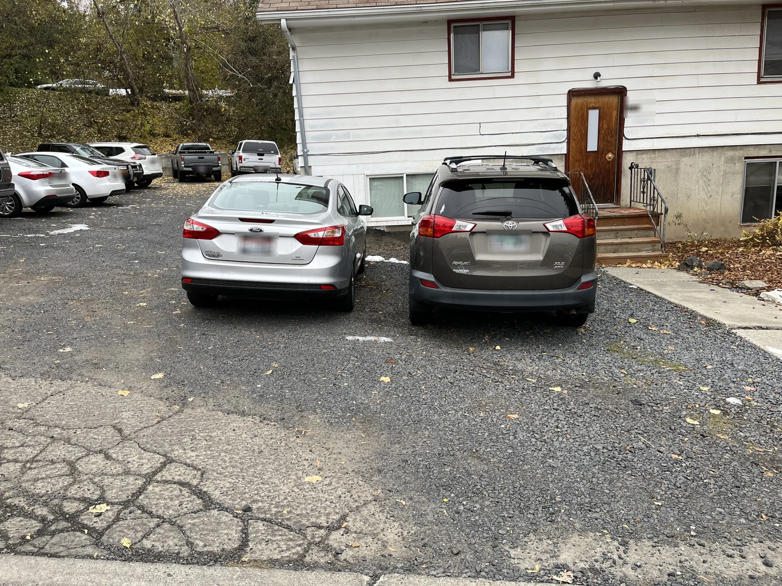 Silver sedan and dark SUV parked outside a white-sided two-story house with a wooden door.