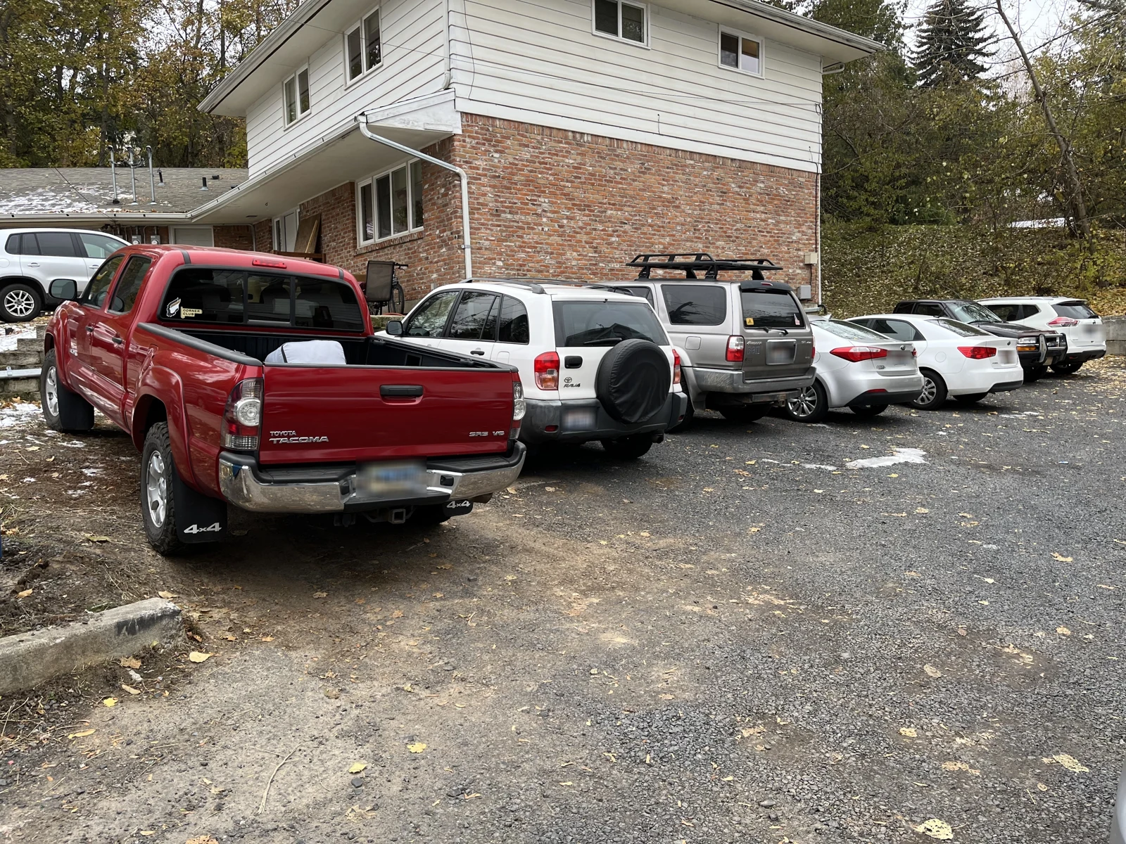 Red pickup truck and a row of SUVs and cars parked beside a brick and white-sided building.