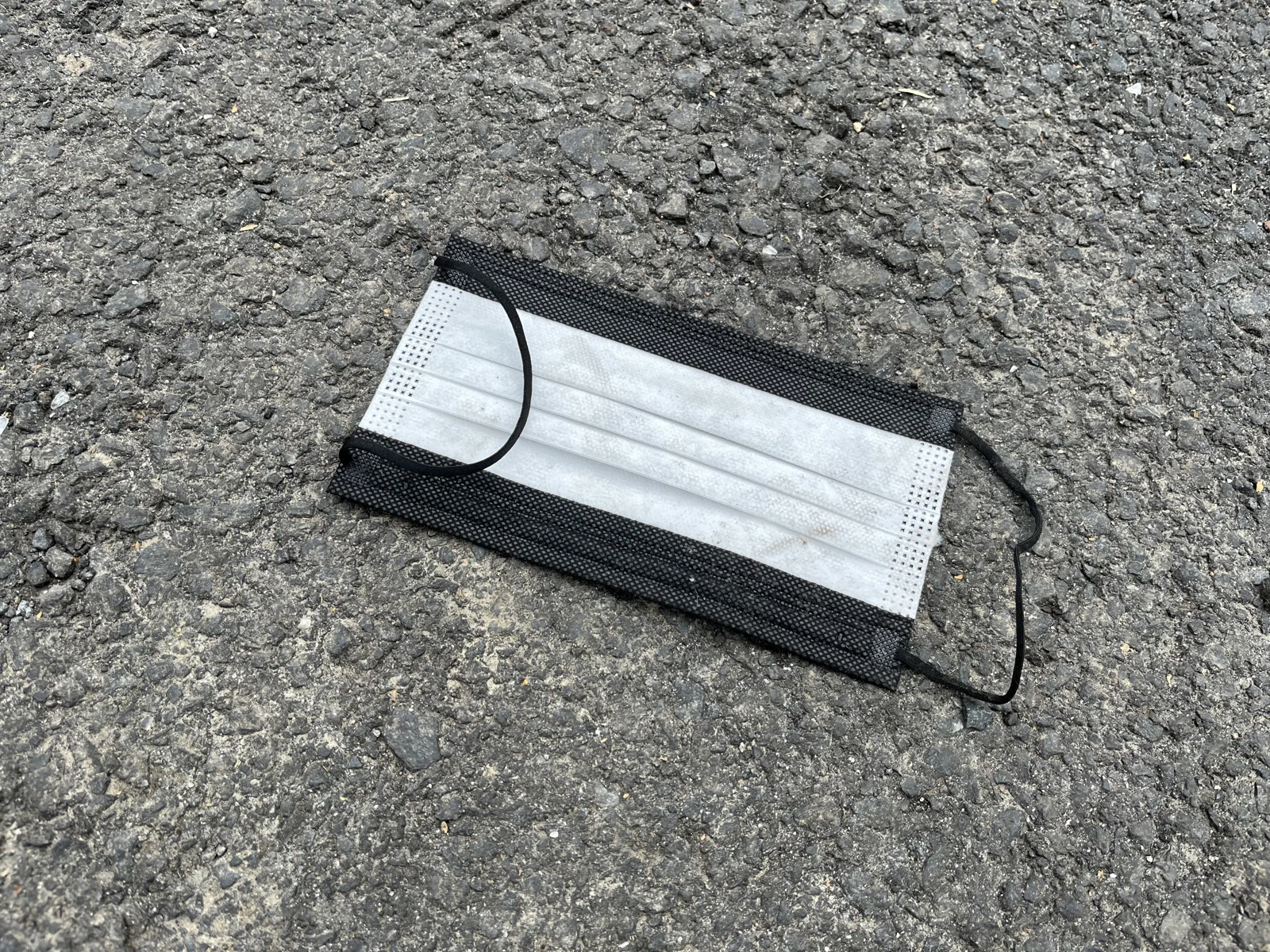 Close view of a black-and-white pleated disposable face mask with black ear loops on asphalt.