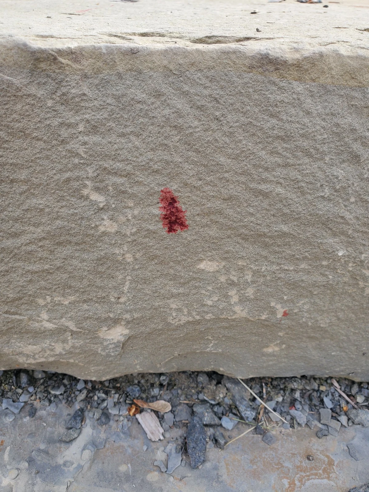 Close view of a triangular reddish mark on the vertical face of a pale stone block.
