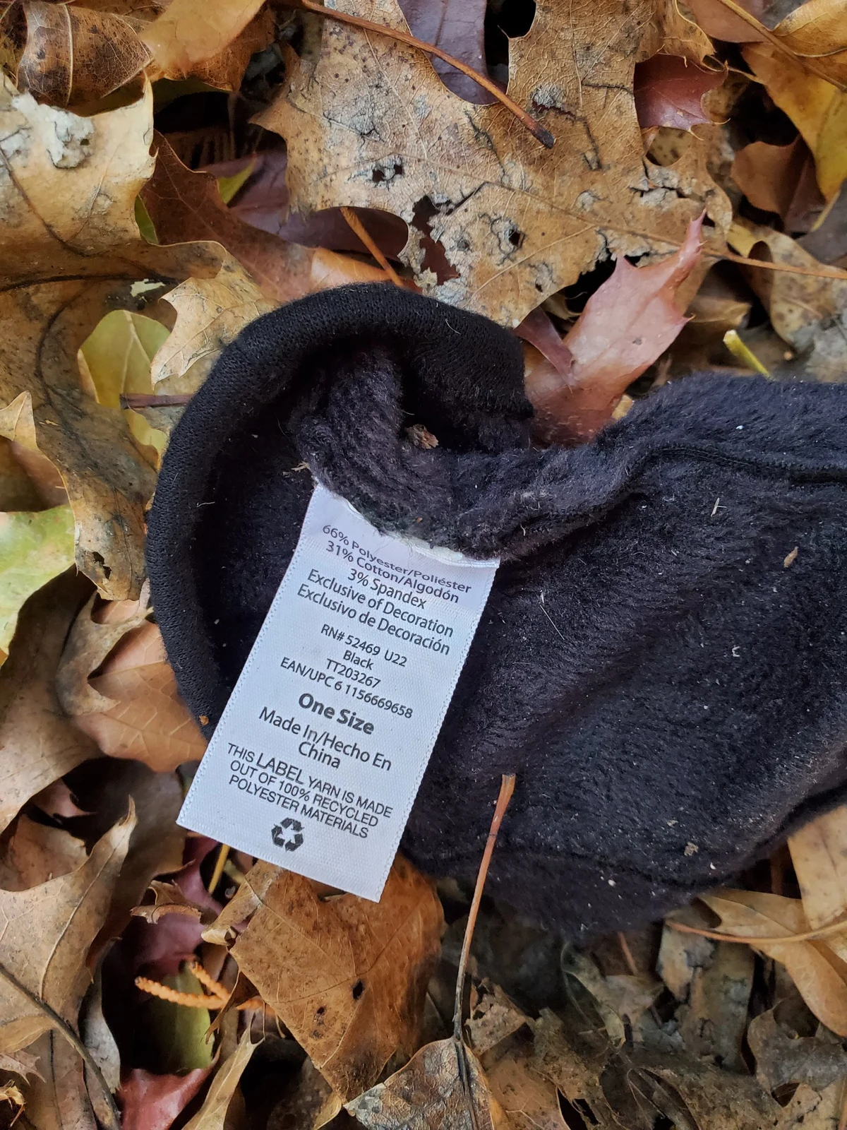 Close view of a white care label inside a dark knitted cap lying among fallen leaves.