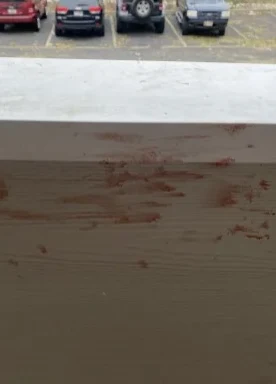 Reddish smears on a pale balcony railing, with parked vehicles beyond it.