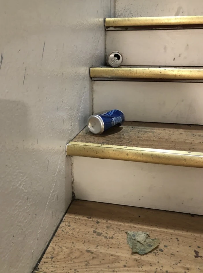 Worn wooden stair treads with metal edges, beverage cans and a small piece of material on a lower step.