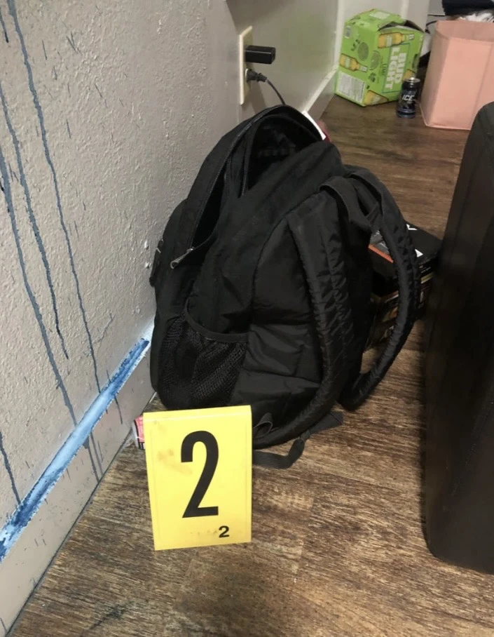 Black backpack beside yellow evidence marker 2, a wall with blue drips and boxes on the floor.