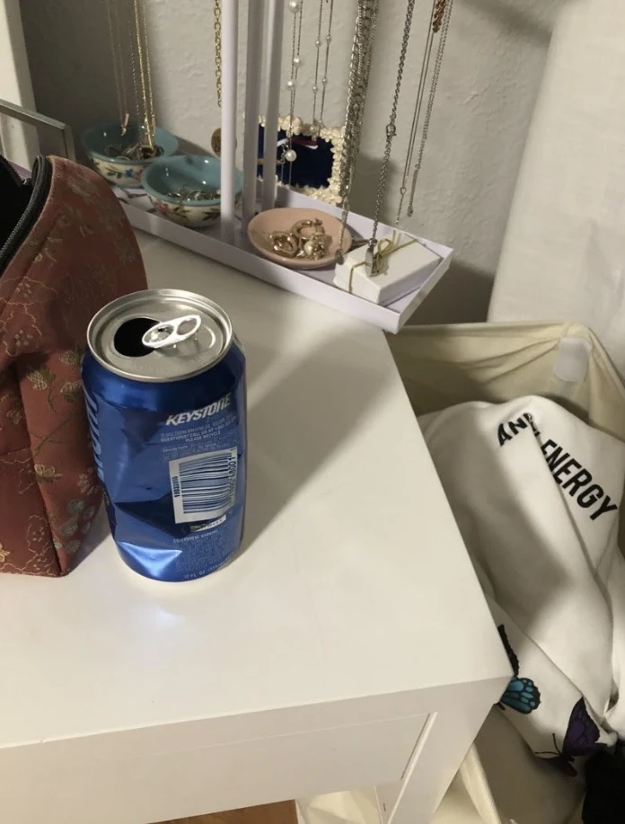 Open blue beverage can on a white vanity desk beside a jewelry stand, pouch and laundry hamper.