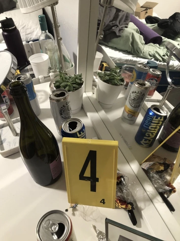 Bottles and open beverage cans on a mirrored vanity beside yellow evidence marker 4.