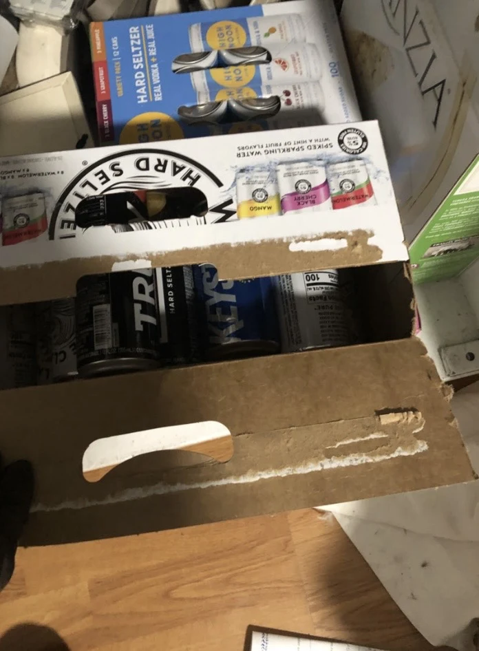 Open cardboard beverage cartons holding assorted cans on a wooden closet floor.