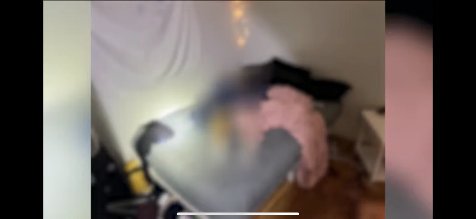 Soft-focus phone screenshot of a bedroom with gray bedding, a pink blanket and a bright flashlight spot.
