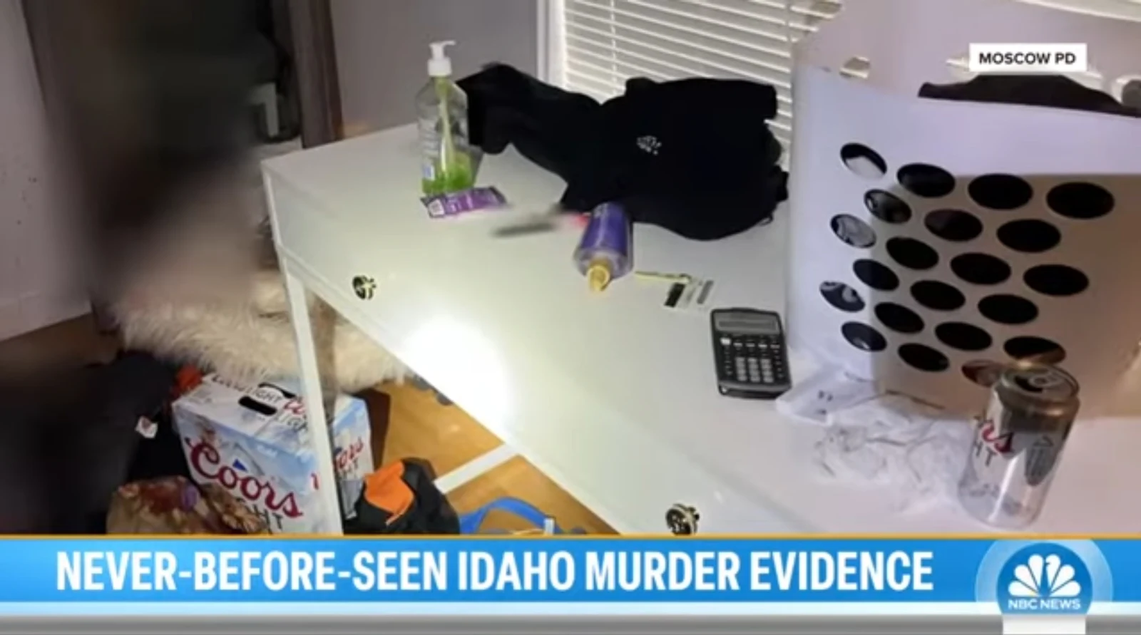 News screenshot of a white desk with a laundry basket, clothing, bottles, a calculator and beverage carton below.