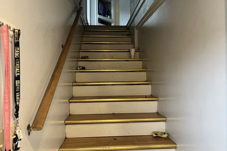 Indoor staircase with wooden handrail, metal stair edges, cans, a cup and a small cloth-like item on the steps.