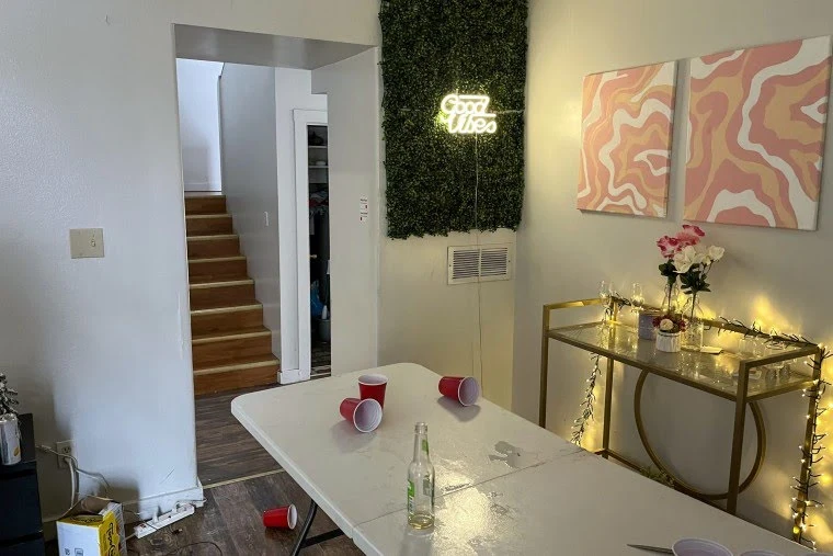White table with red cups and a bottle, glass console with string lights, abstract wall art and an illuminated Good Vibes sign beside stairs.