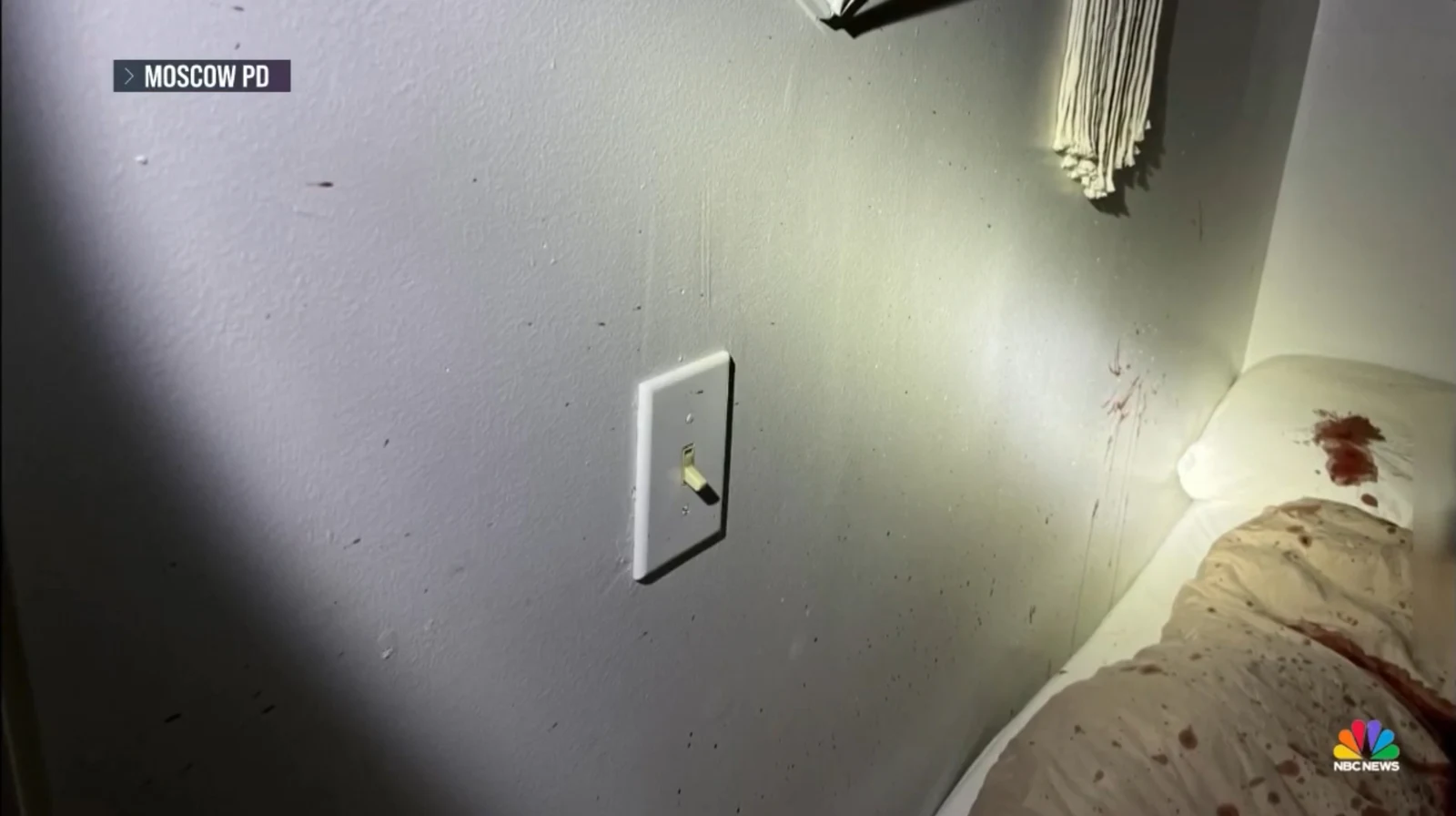 News image of a wall and light switch beside stained bedding, with reddish marks and small dark spots.