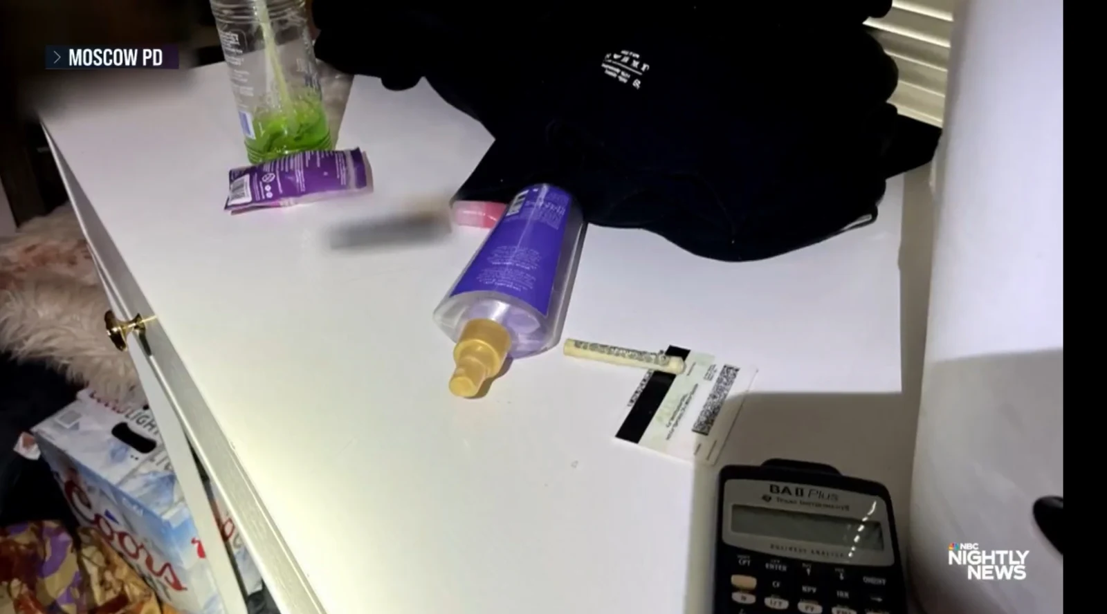News close-up of a white desk with a purple spray bottle, black clothing, measuring strips and a calculator.