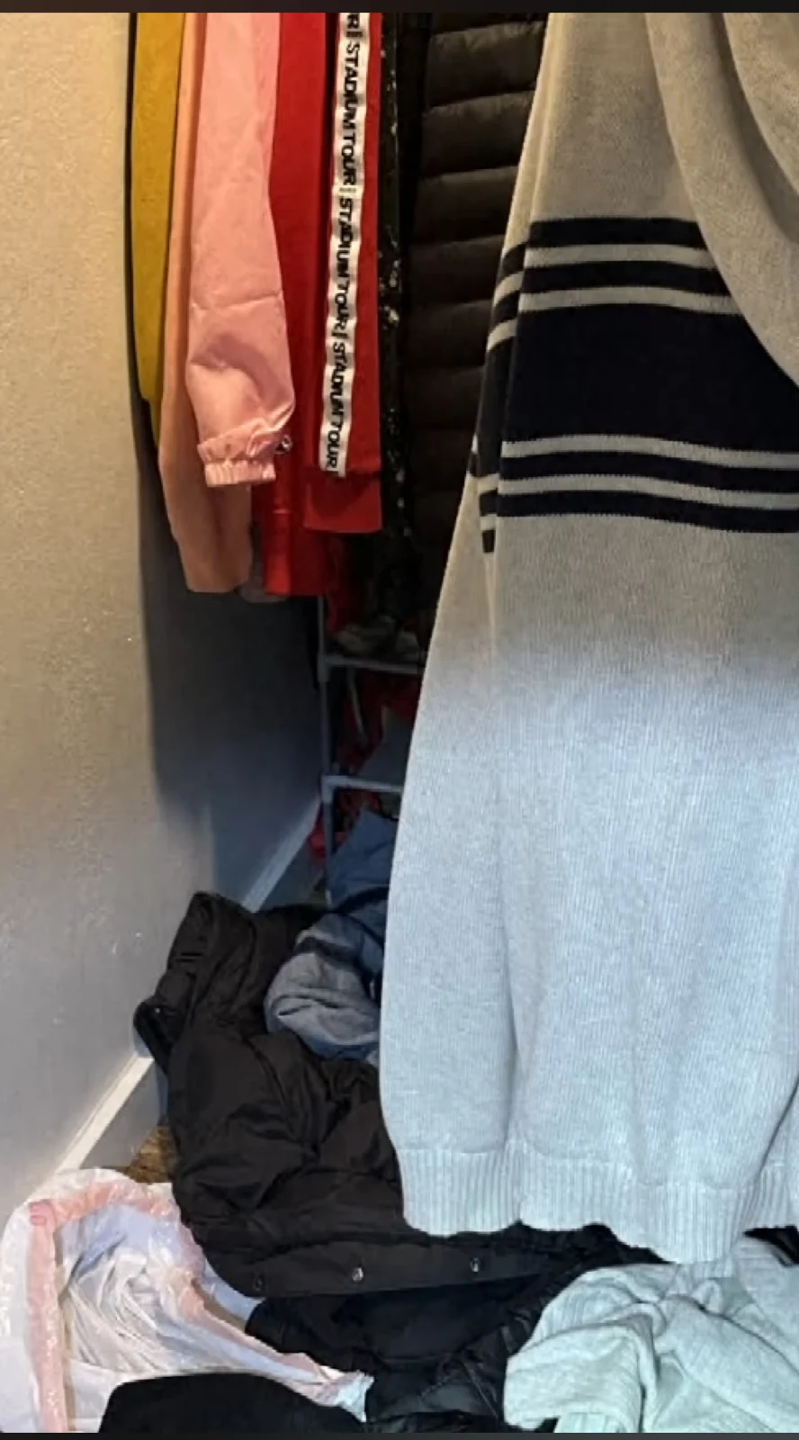 Closet with hanging jackets and a striped garment above a pile of clothing.