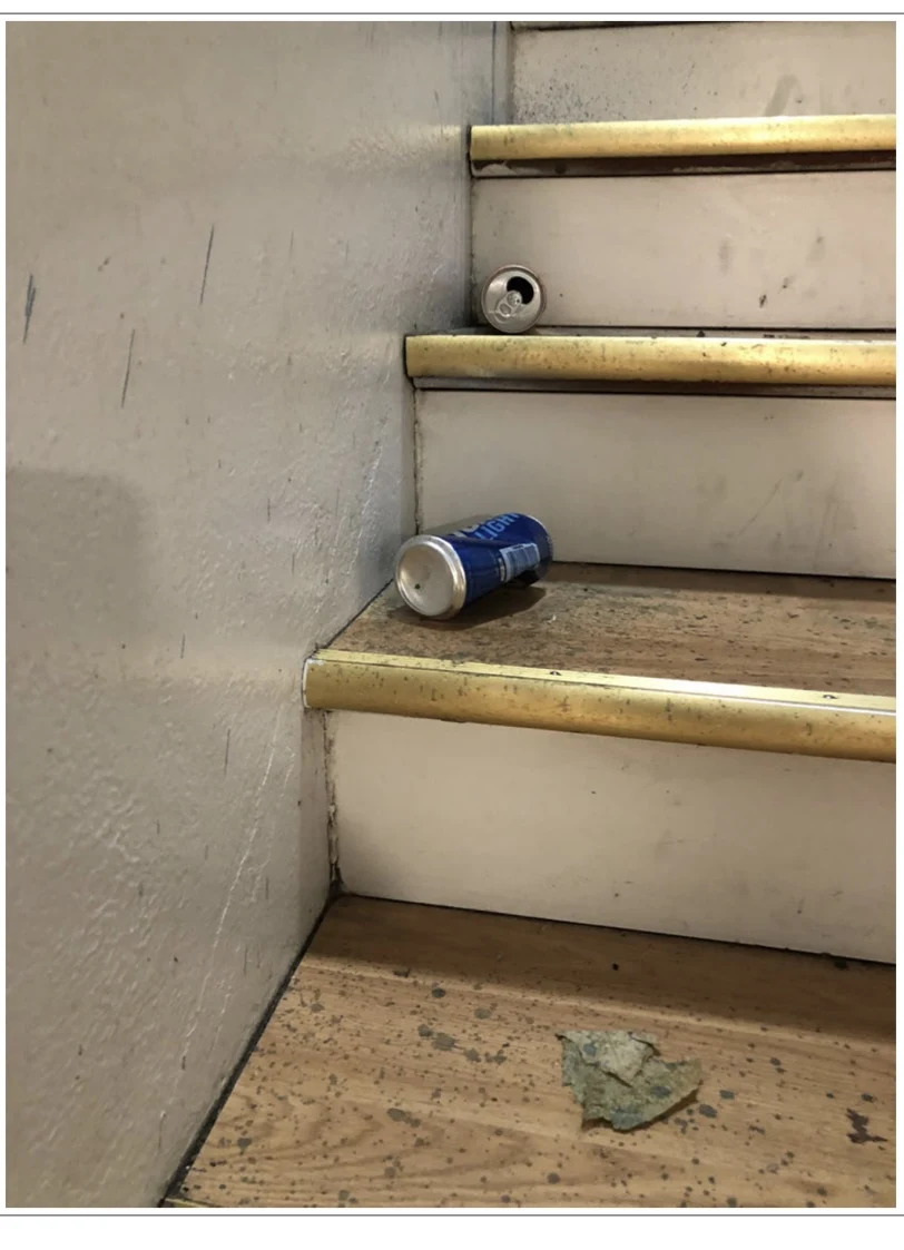 Beverage cans and a small material fragment on worn wooden stairs with metal edges.