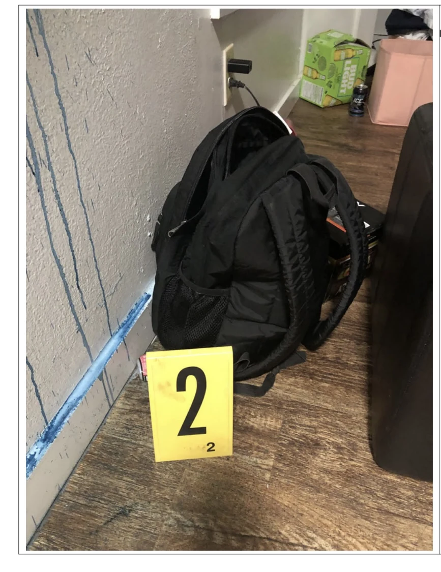 Black backpack beside yellow evidence marker 2 and a wall with blue drips.