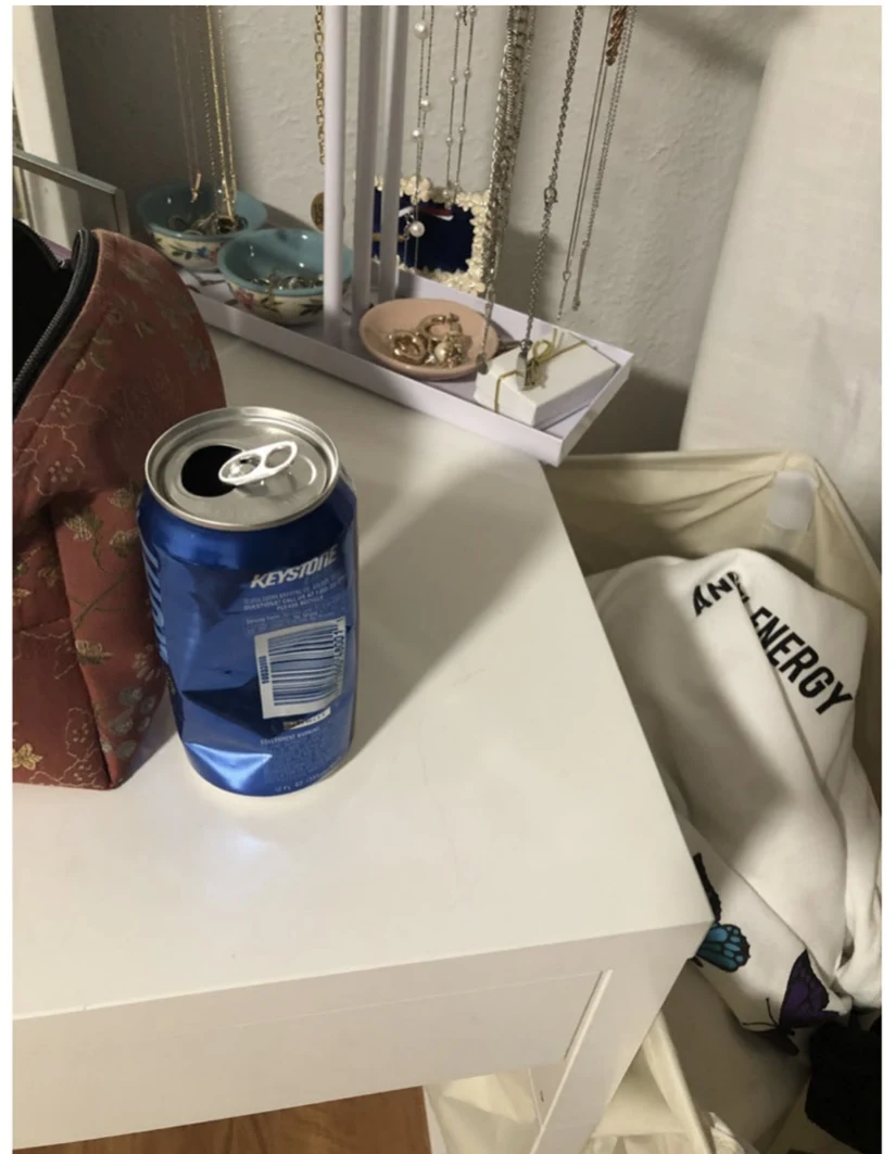 Open blue beverage can on a white vanity next to a pouch, jewelry stand and laundry hamper.