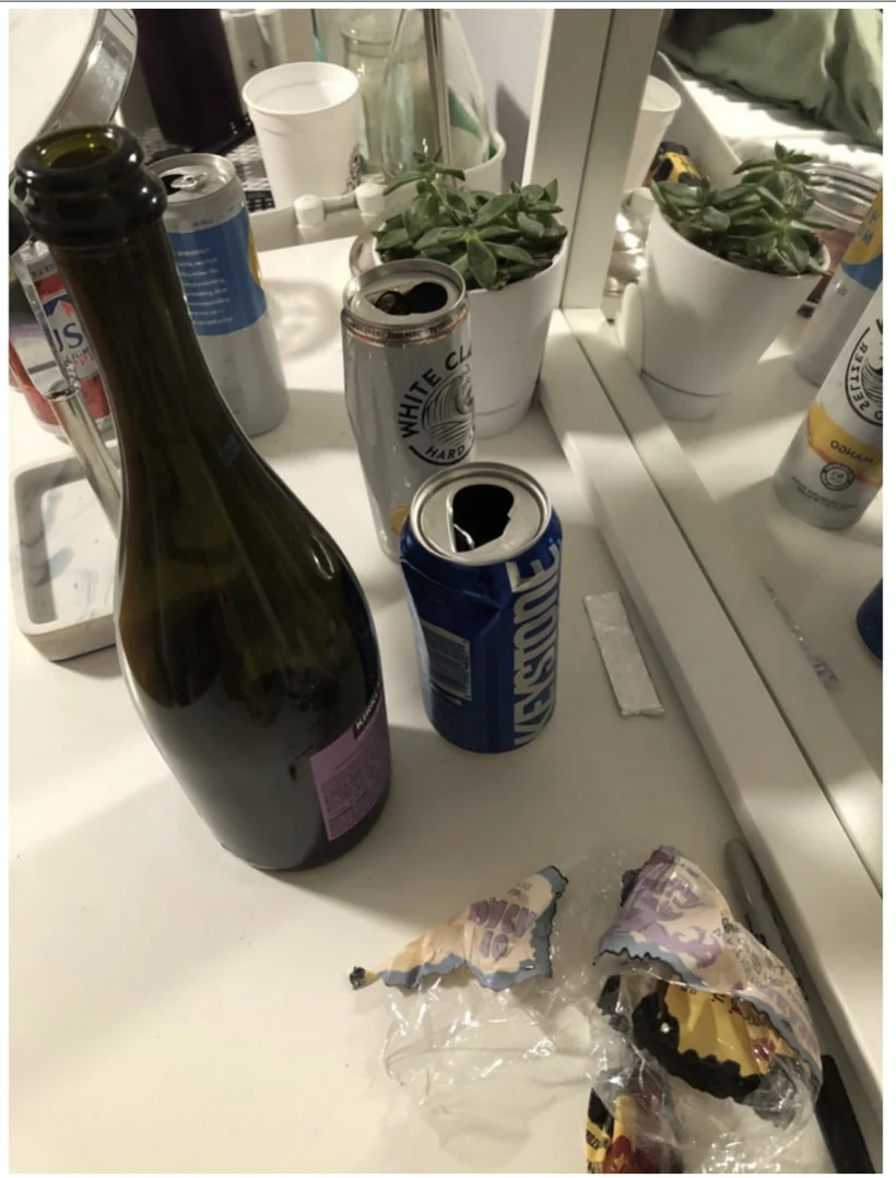 Bottles, beverage cans, a succulent and wrappers on a white mirrored vanity.