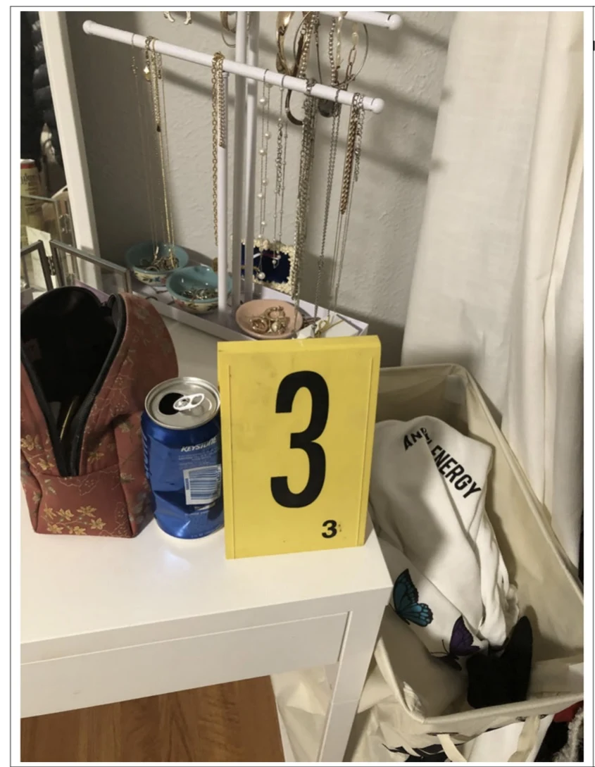Blue can and pouch on a vanity beside yellow evidence marker 3, jewelry and a laundry hamper.