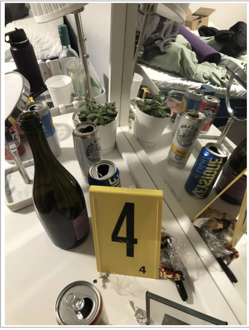 Bottles and open cans on a mirrored vanity beside yellow evidence marker 4.